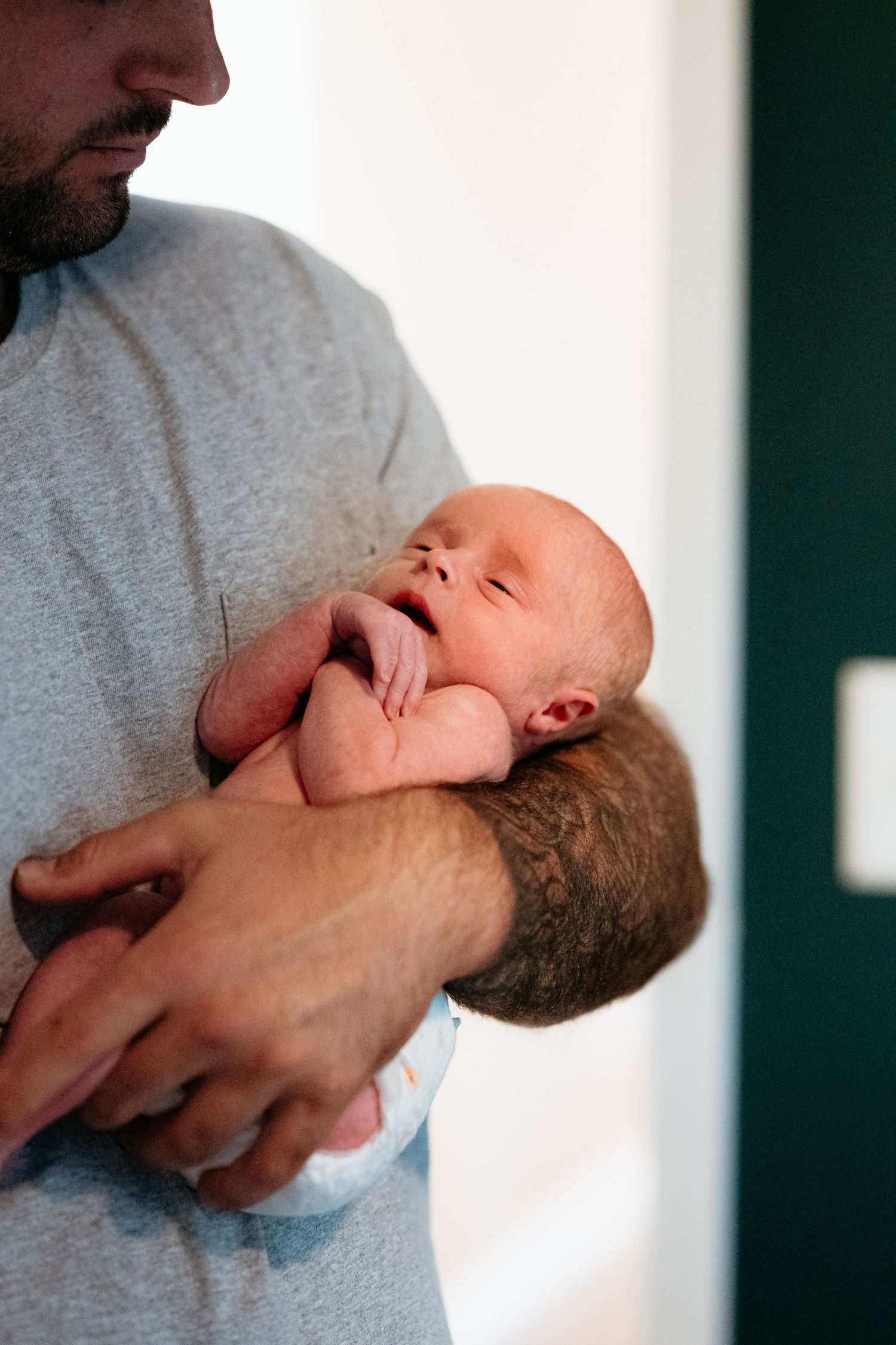 Father in gray shirt gently holding sleeping newborn baby against his chest.
