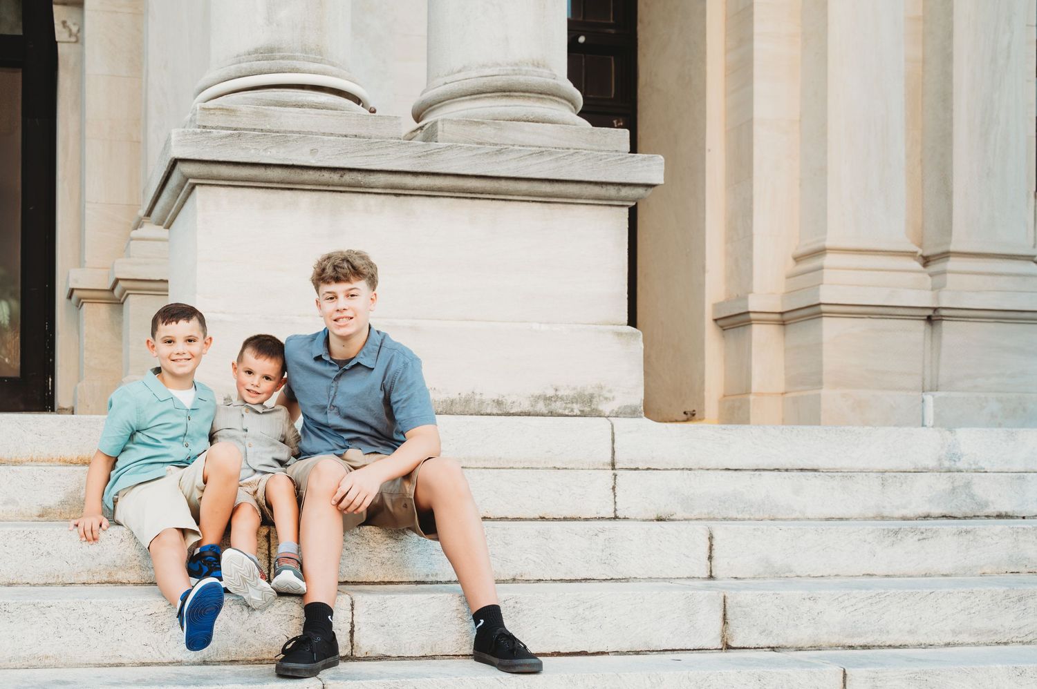 Three brothers pose together smiling on the steps of a grand stone building.
