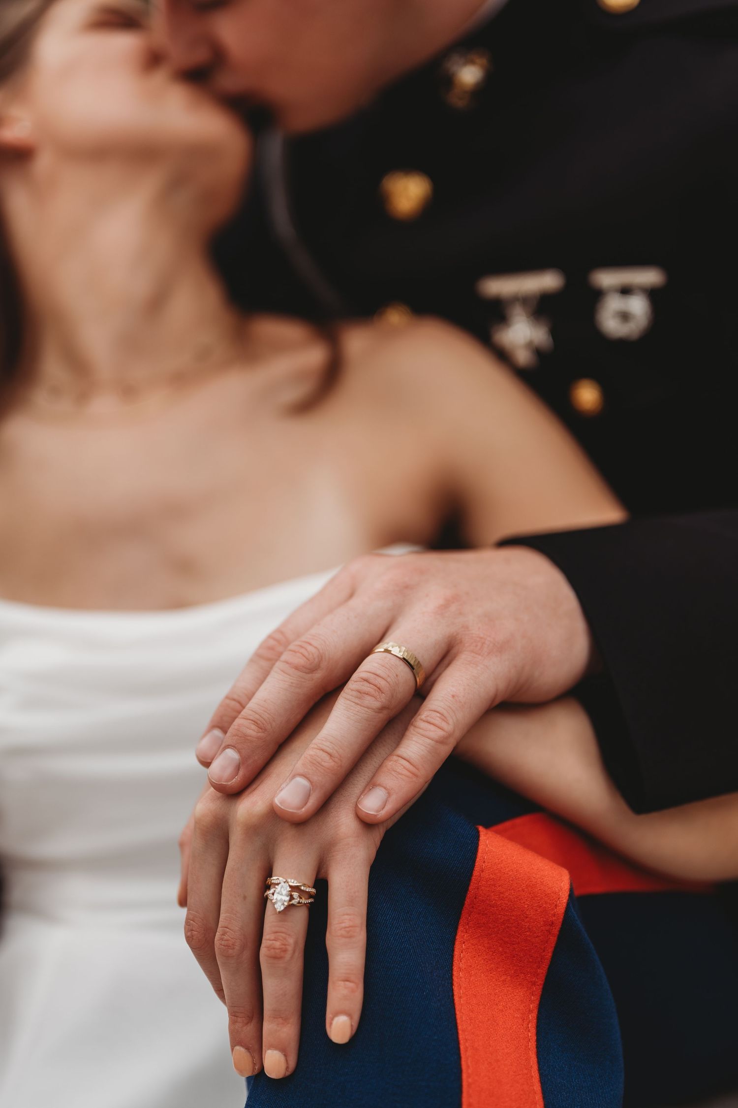 Military wedding couple kissing while displaying wedding rings, bride in white dress, groom in Marine dress uniform.