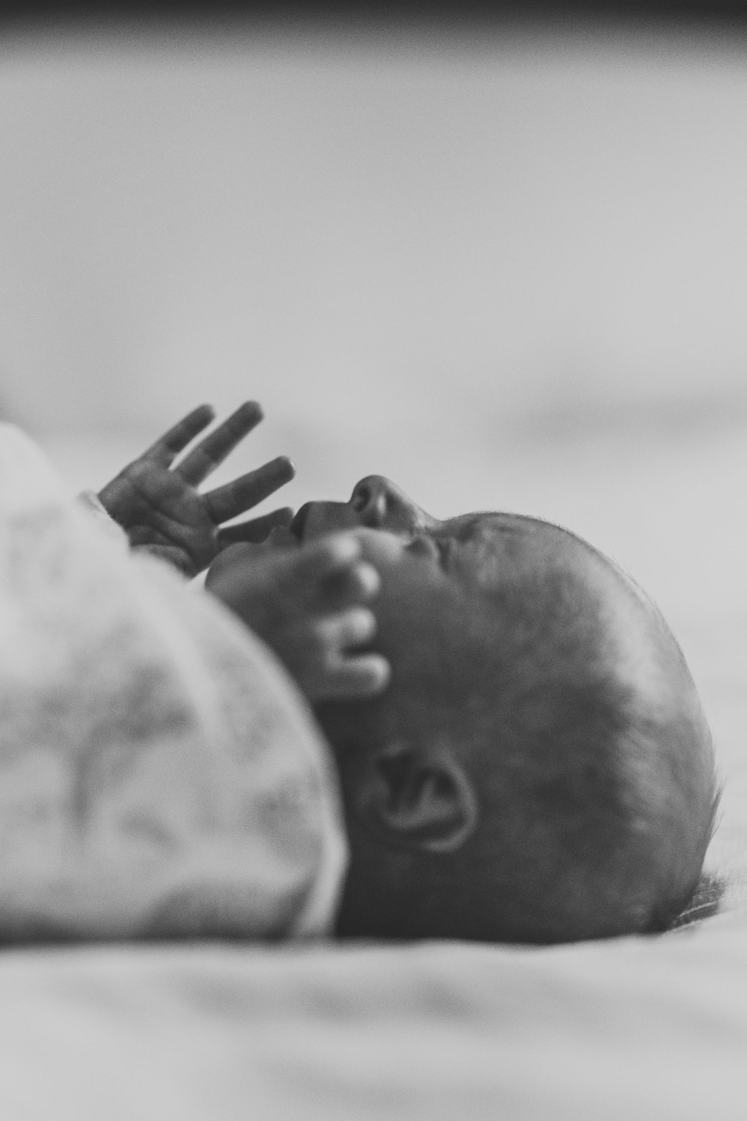 Black and white close-up of newborn baby with tiny hand raised beside face.
