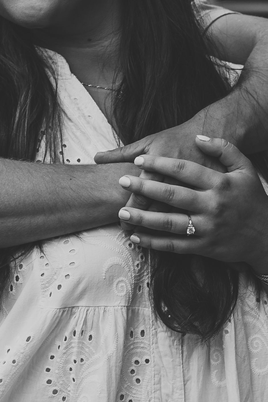 Black and white photo of a couple holding hands, woman wearing a diamond engagement ring, in a romantic embrace.