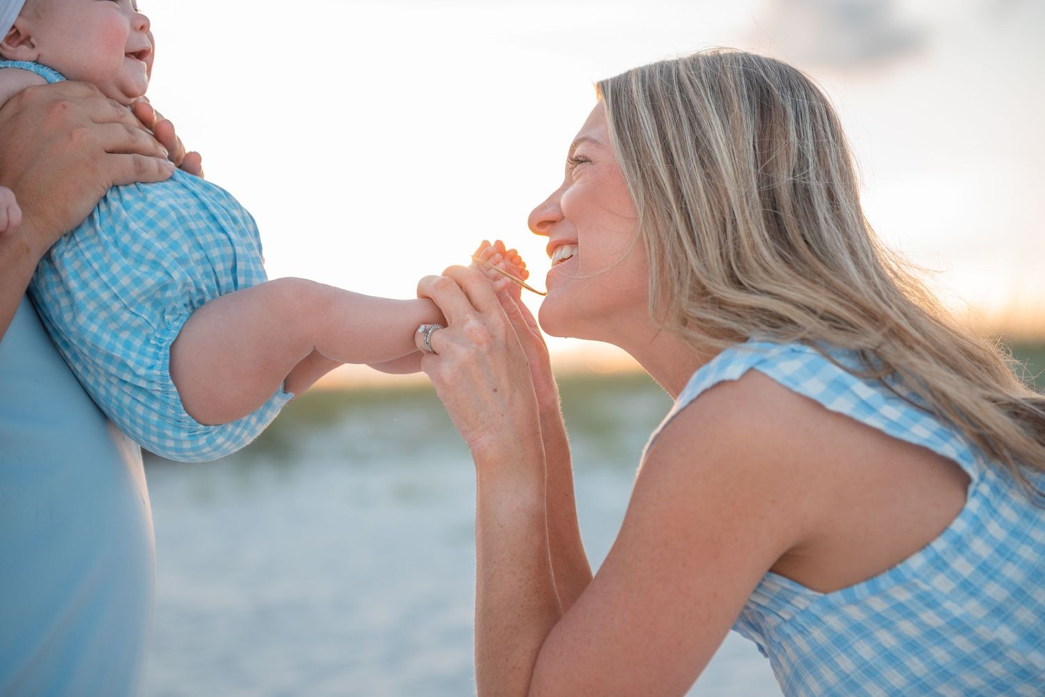 Smiling mother kissing her baby girls hand while dad holds her on the beach.