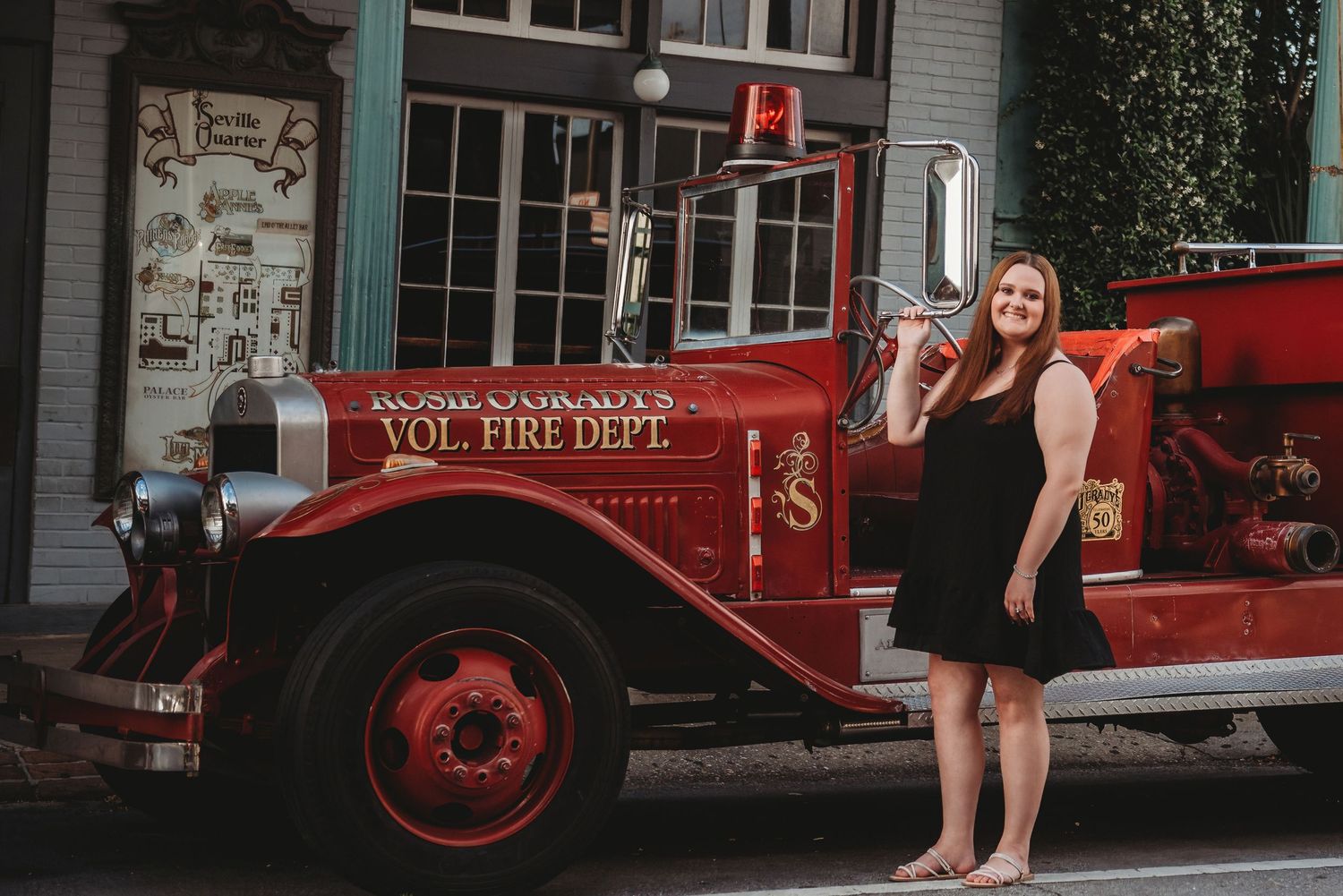 A woman in a black dress poses beside a vintage red volunteer fire department truck.