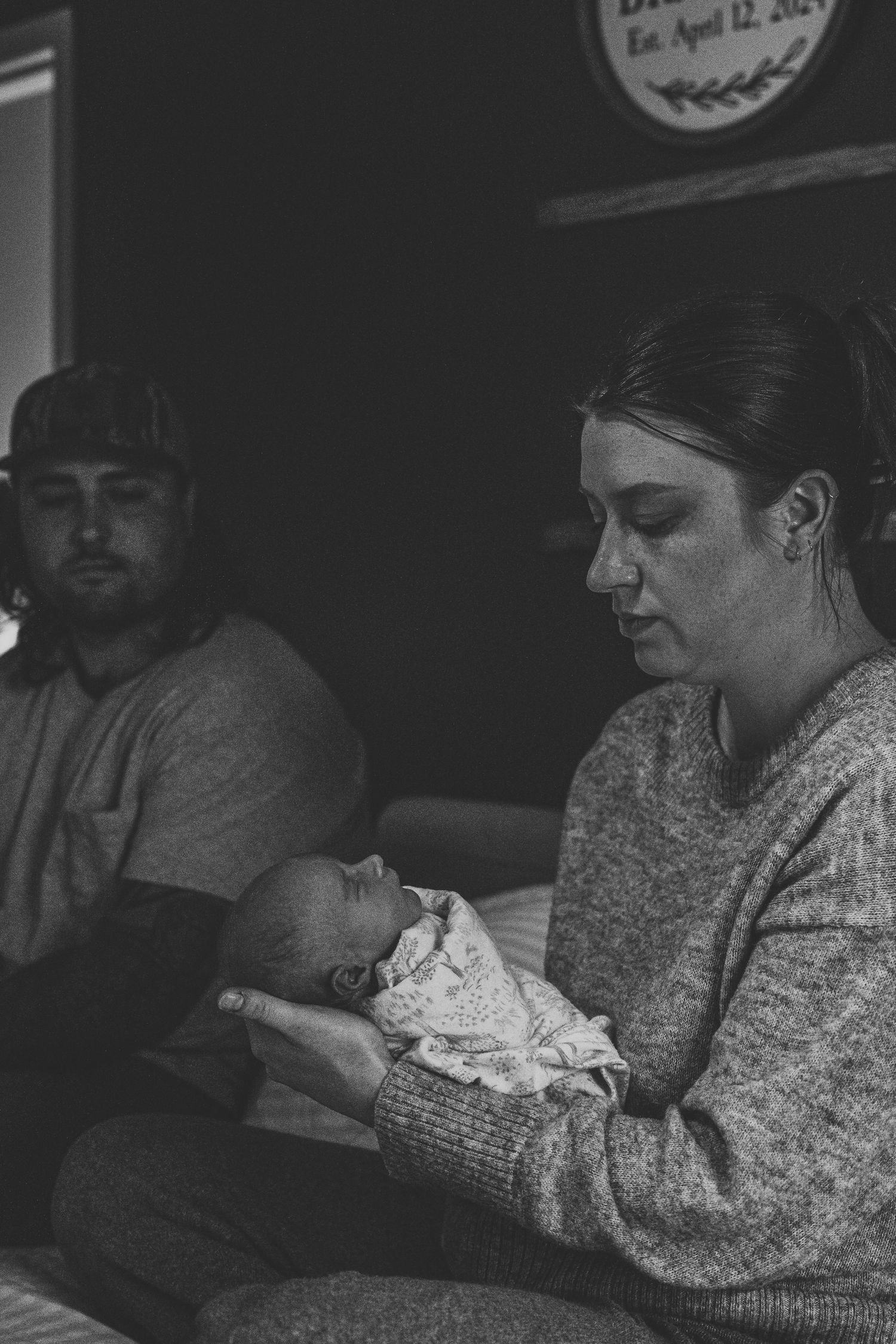 Black and white photo of new parents holding their newborn baby at home.