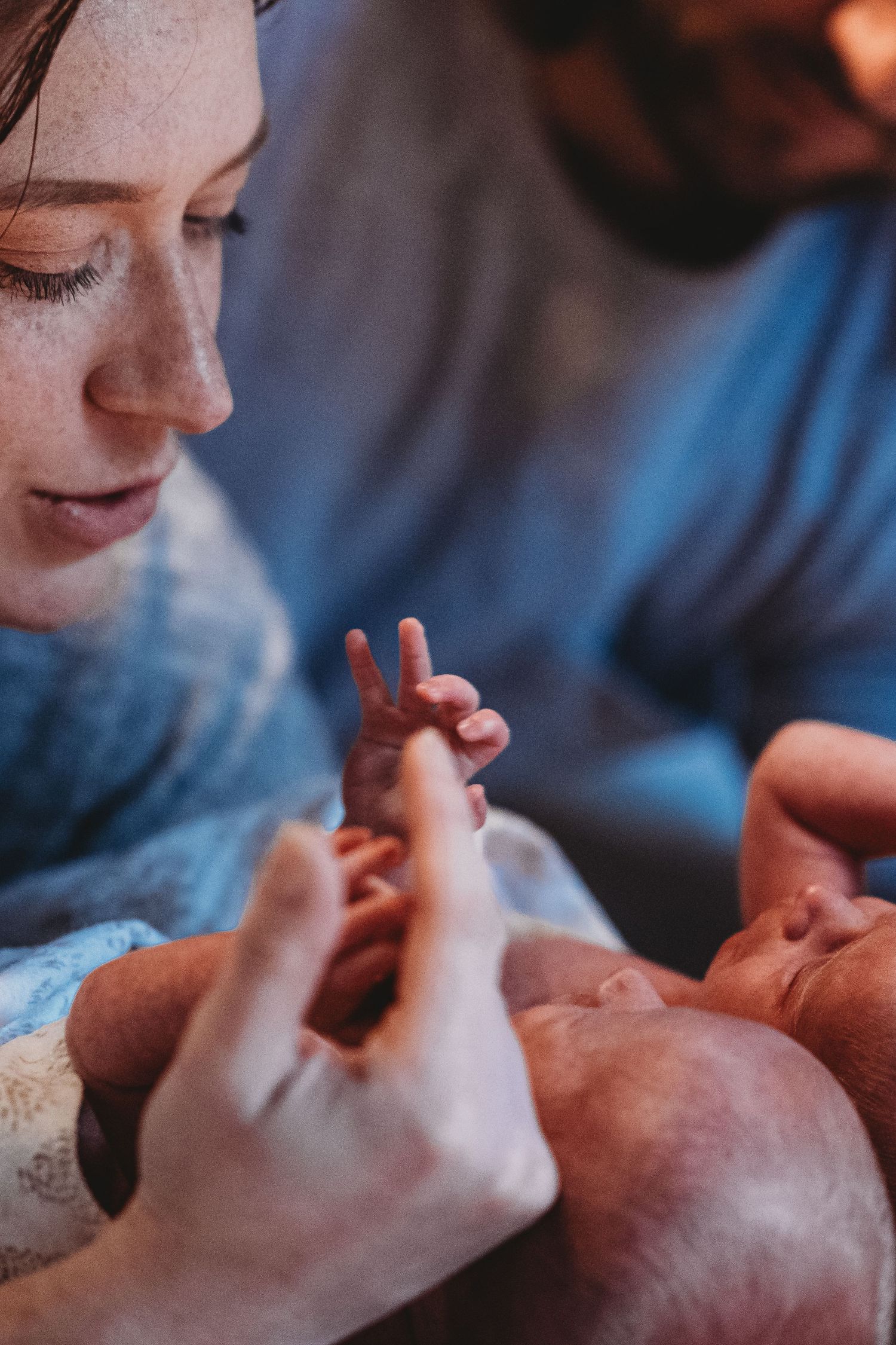 Mother gazing lovingly at newborn baby while holding tiny fingers close to her face.