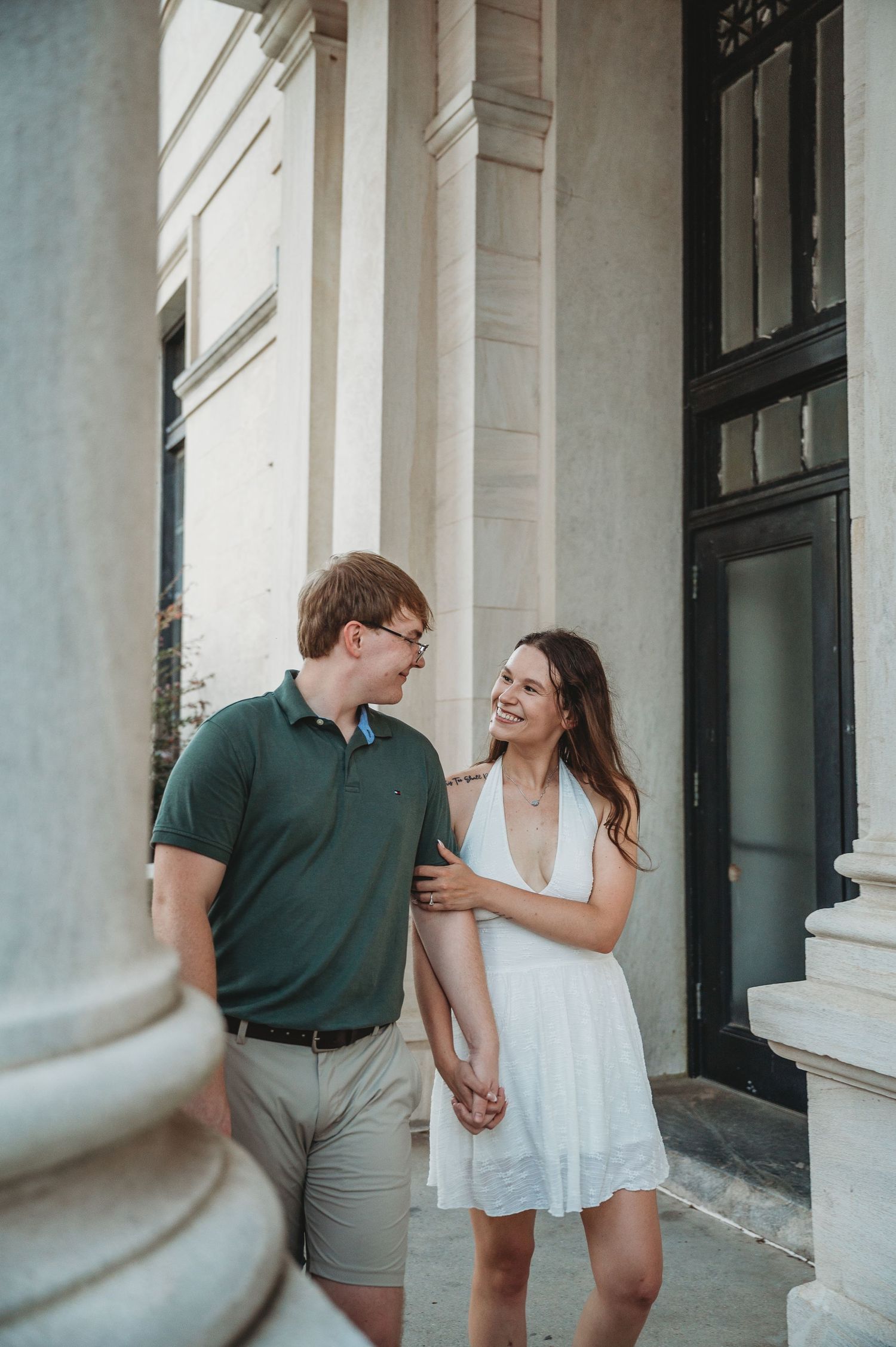 Happy couple holding hands and smiling at each other beside elegant white columns of a classic building.