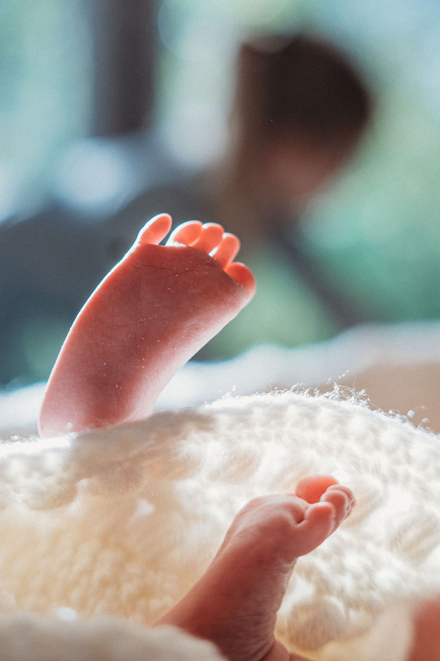 Tiny newborn baby feet resting on a soft white blanket.