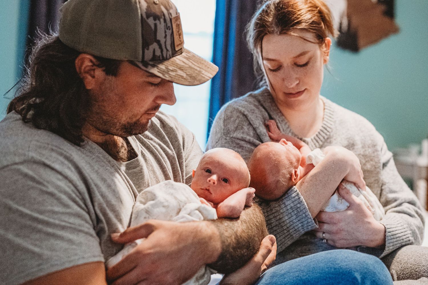 New parents sitting together each holding one of their newborn twin babies.