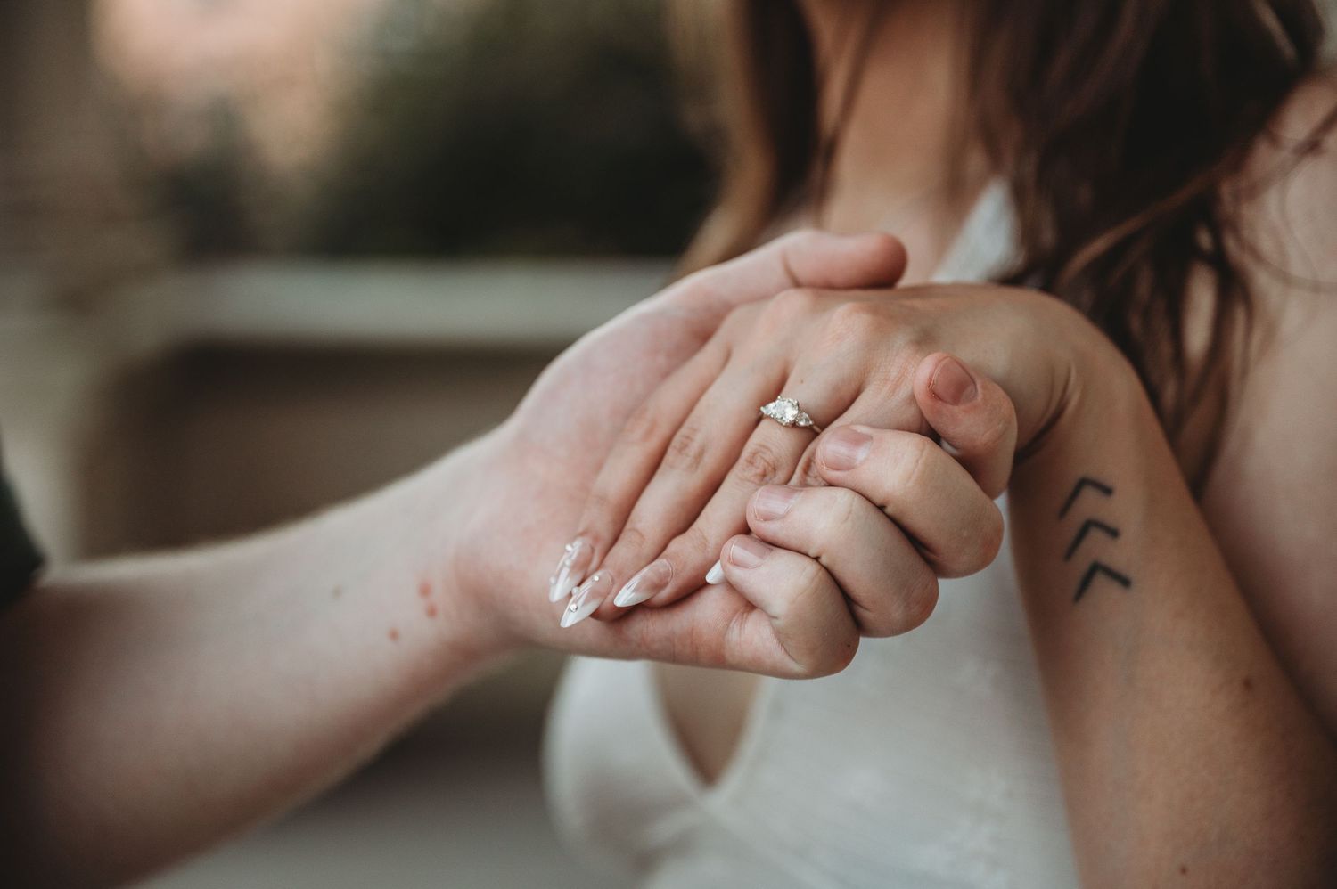 Close-up of couple holding hands showing engagement ring and arrow tattoo on wrist.
