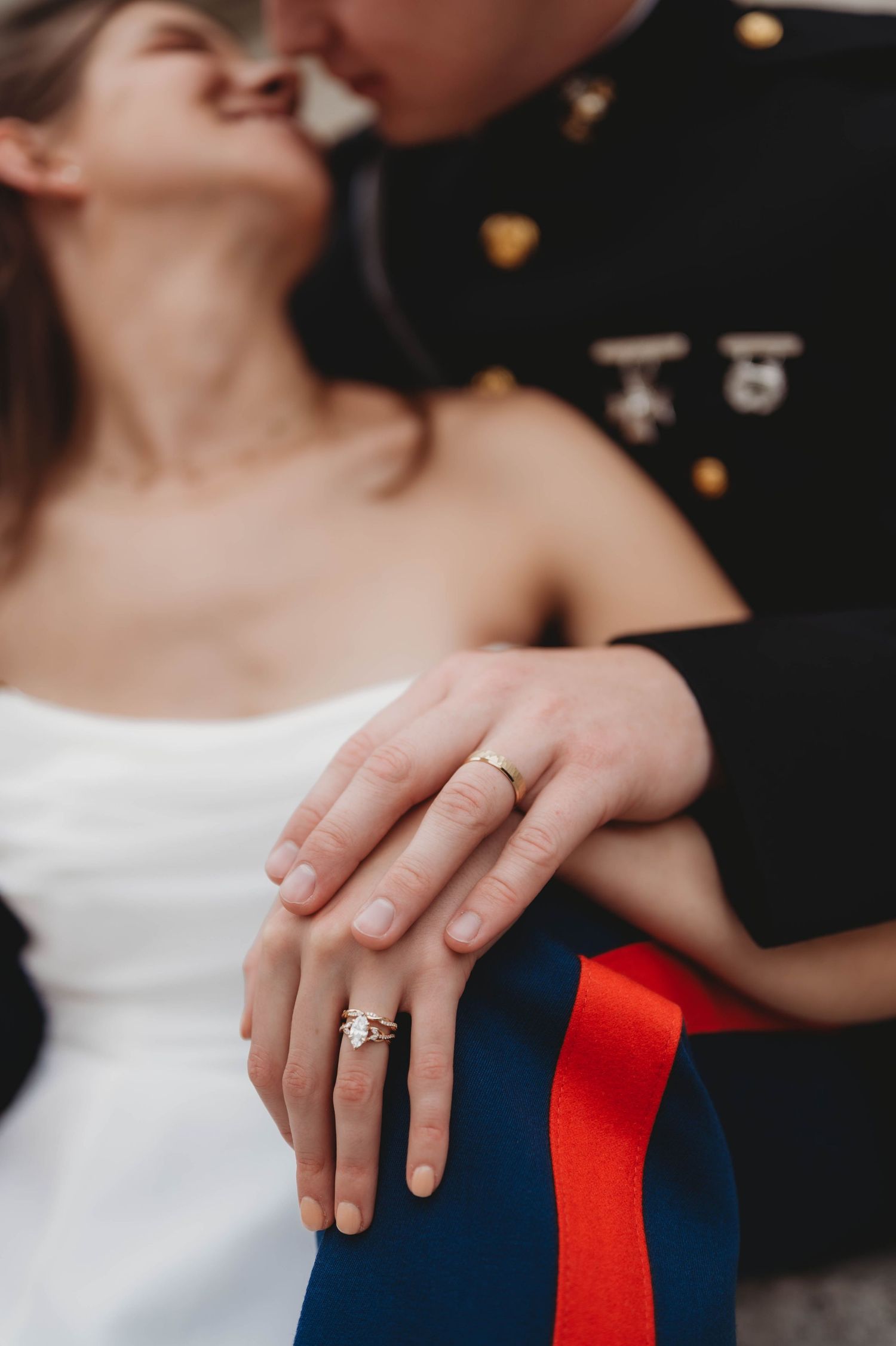 Close-up of bride's engagement ring and wedding band as couple kisses in Marine dress uniform.