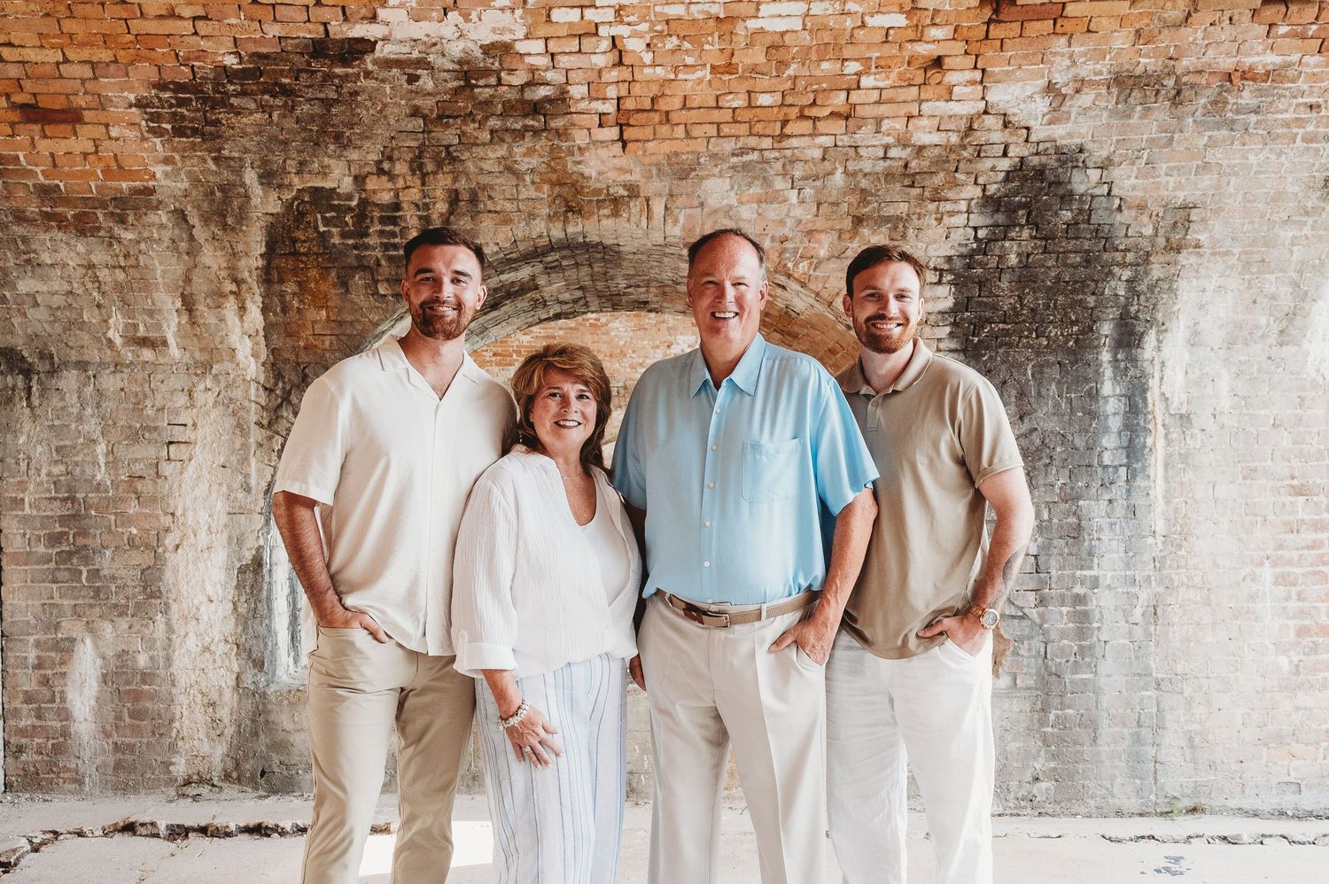 Family portrait of four people standing together against an aged brick wall at a historic site.