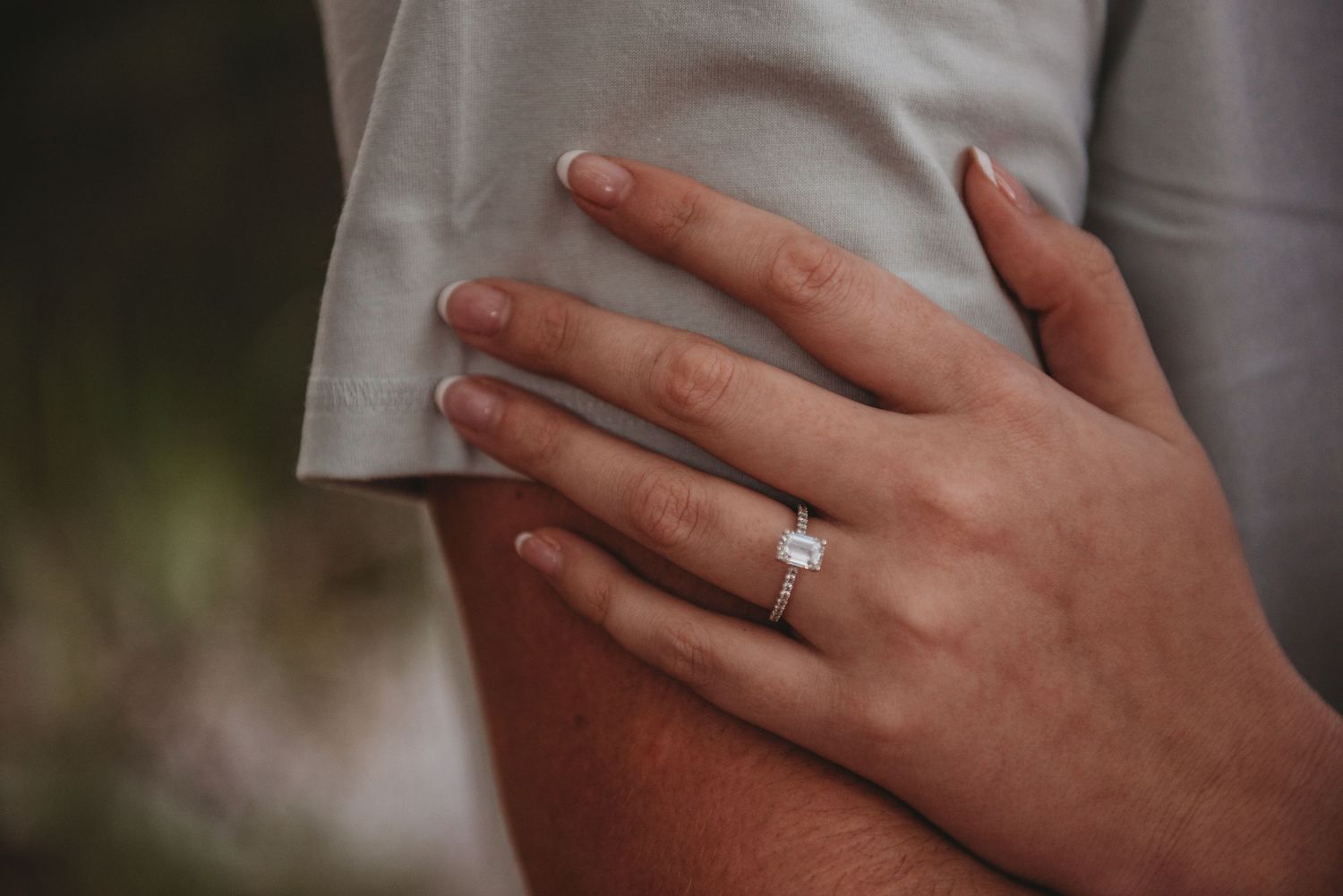 Close-up of a woman's hand wearing a stunning solitaire diamond engagement ring resting on a shirt.