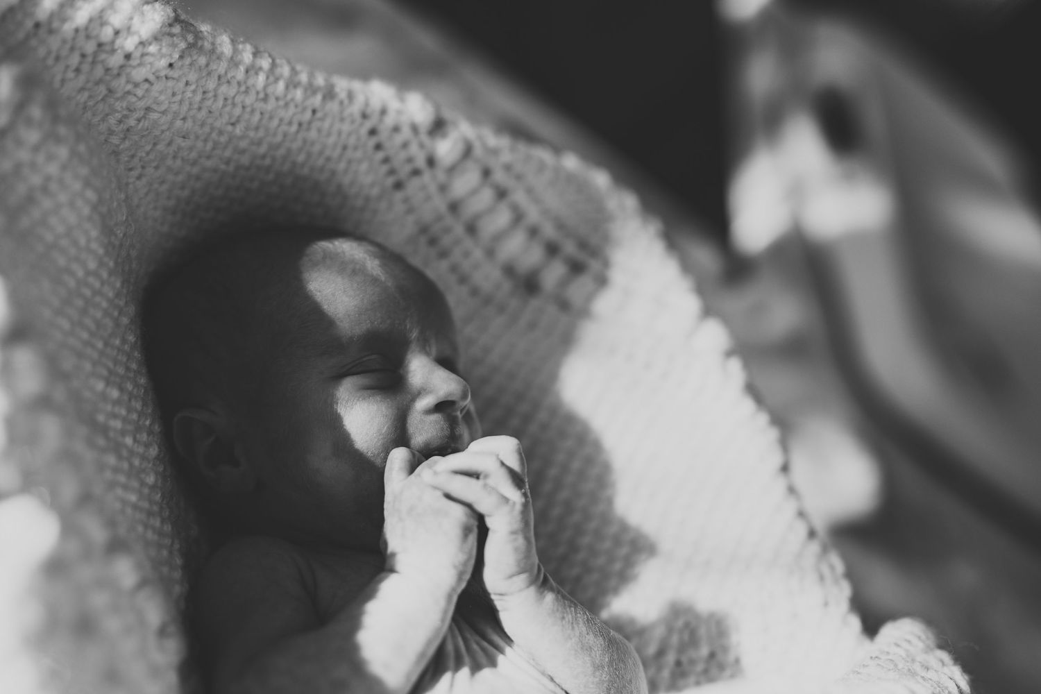 Black and white close-up of a peaceful newborn baby with hands clasped near face.