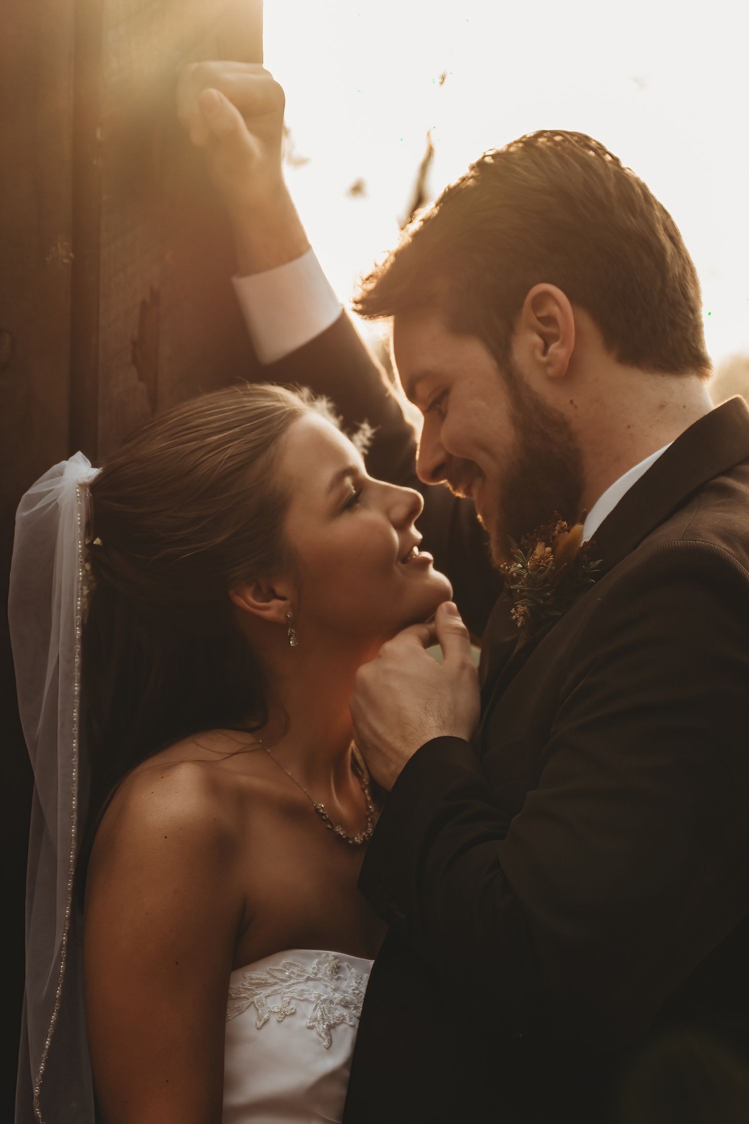 A bride and groom share a romantic golden hour moment, smiling at each other in wedding attire.
