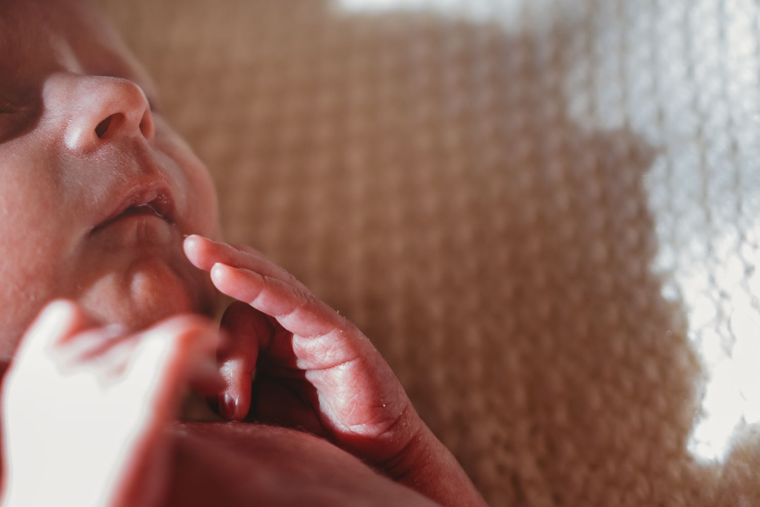 Close-up of a peaceful newborn baby's face with tiny fingers resting on chin.