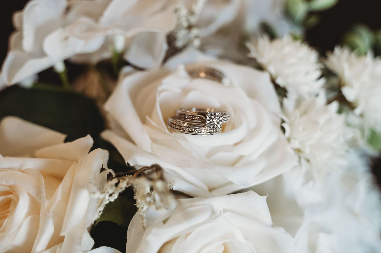 Close-up of wedding rings resting in a white rose bouquet with delicate floral details.