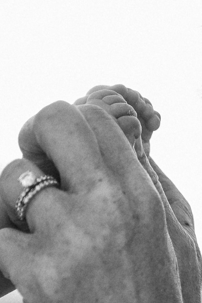 Black and white close-up of adult hands cradling a baby's foot, with a ring visible on one finger.