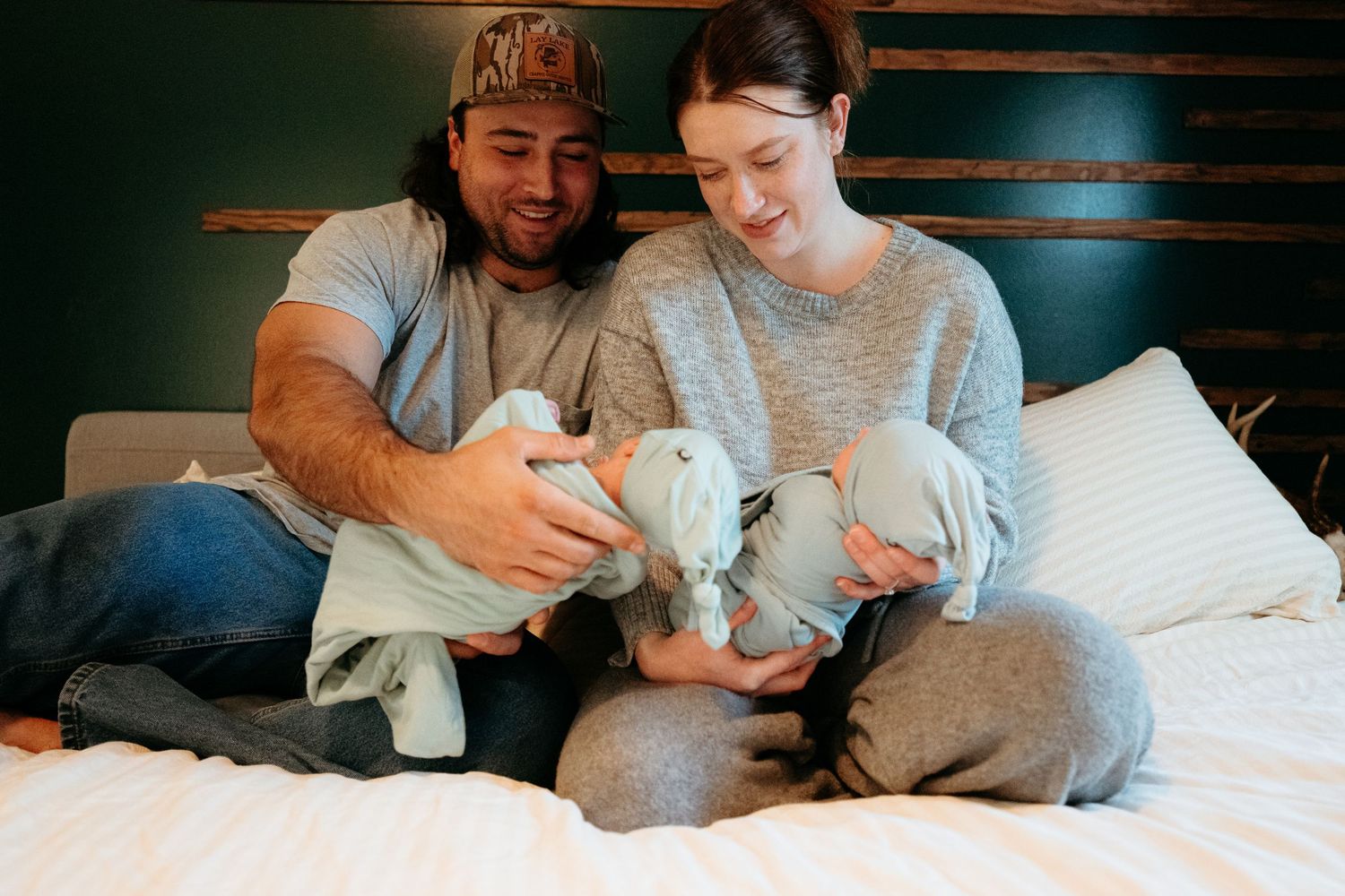 Happy couple sits on bed together holding matching elephant stuffed animals for their new twins.