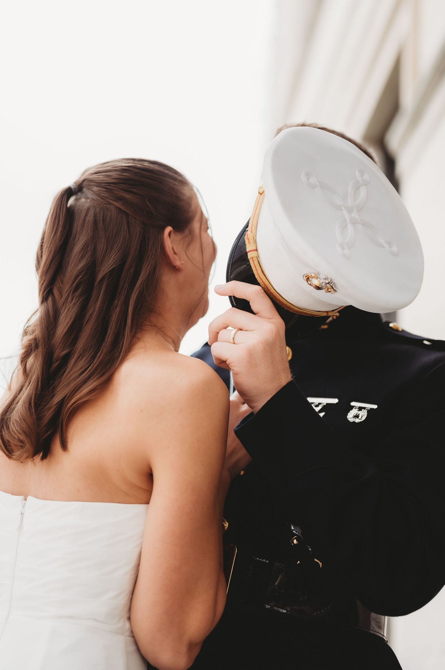Military groom in dress uniform kissing bride in white strapless gown at wedding ceremony.