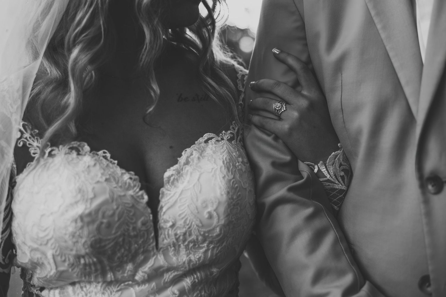 Black and white close-up of bride in lace wedding dress and groom in suit holding hands with wedding rings.