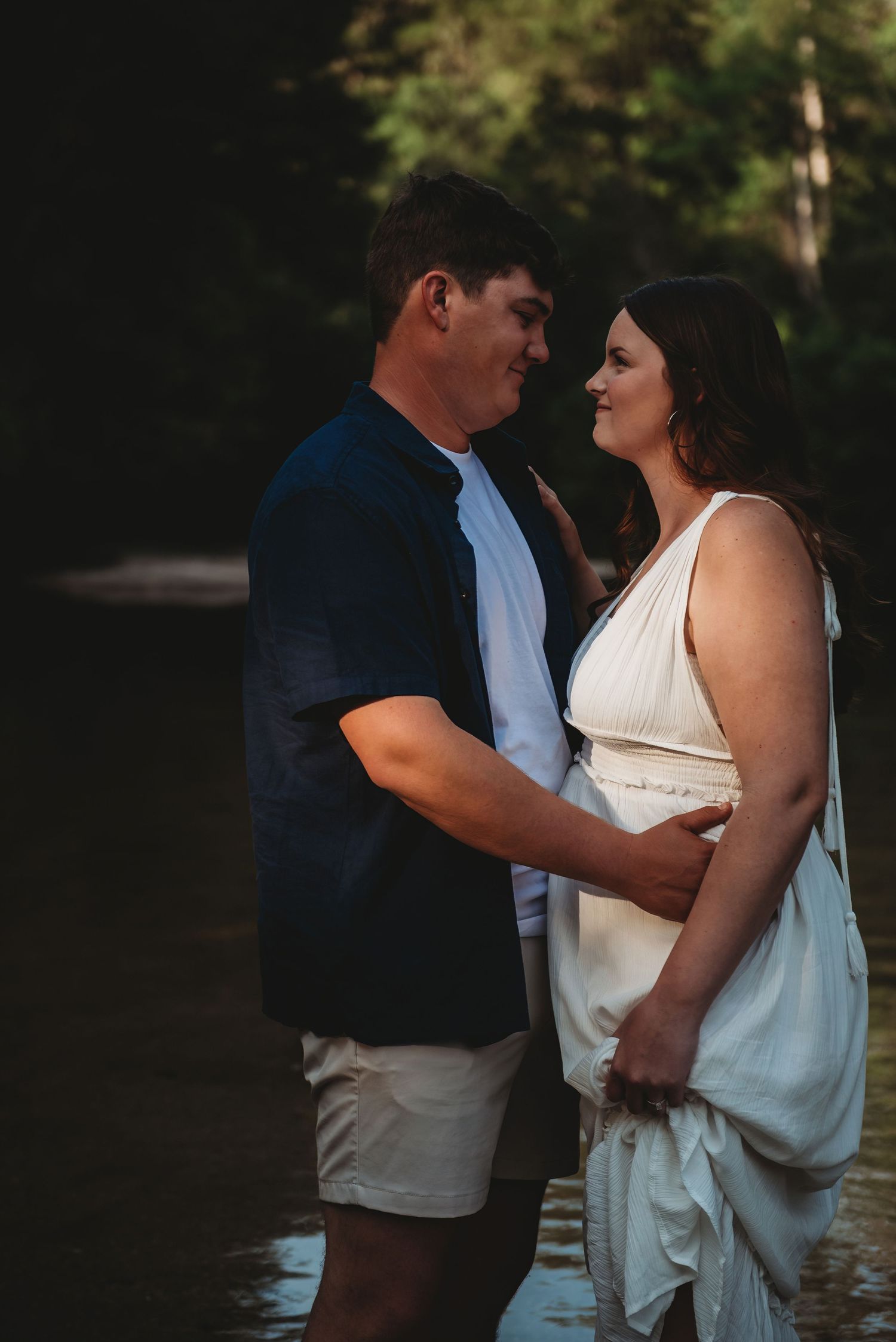 Couple gazing lovingly at each other while standing in a serene forest stream.