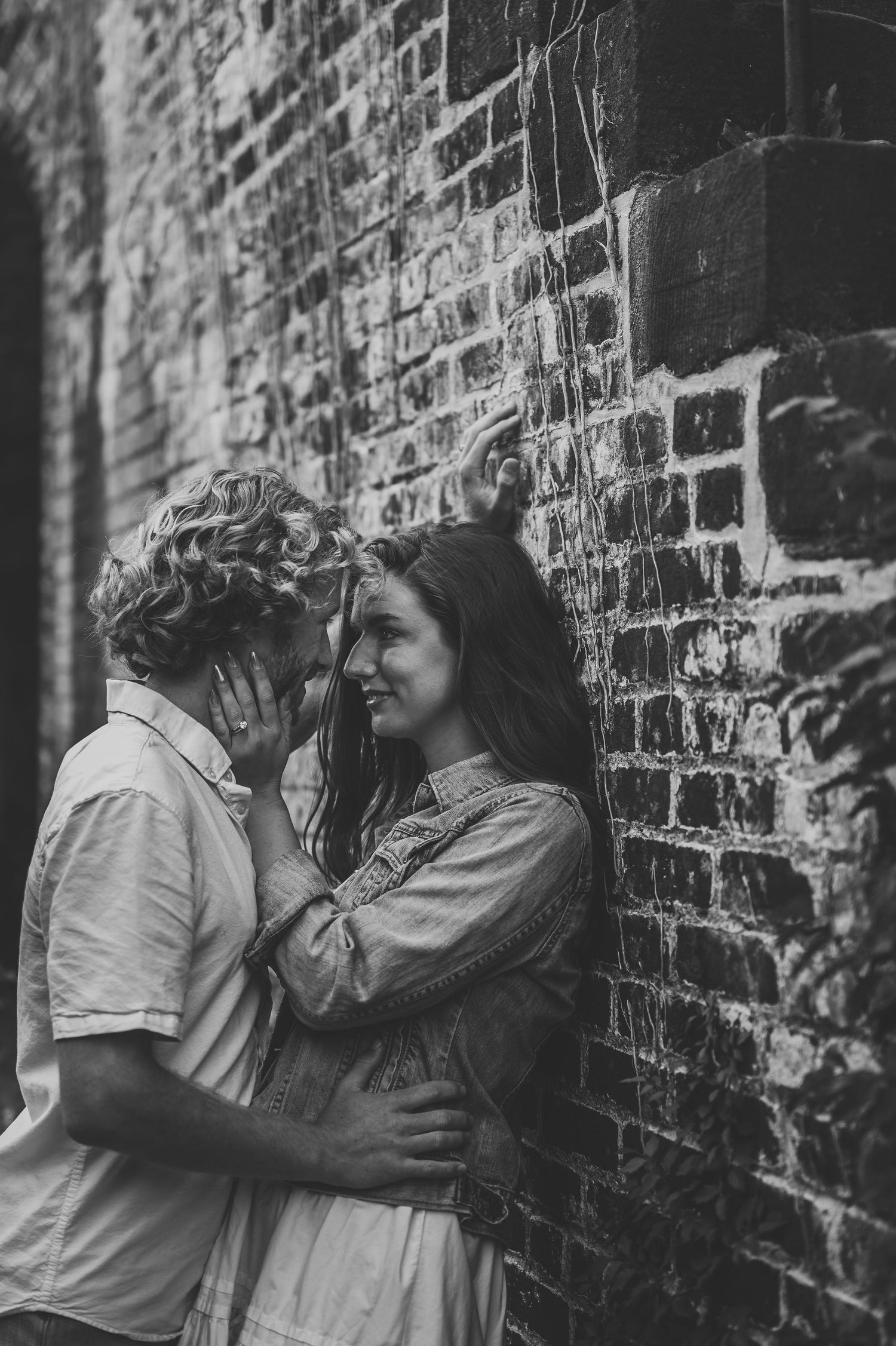 Black and white photo of a romantic couple embracing against a rustic brick wall.