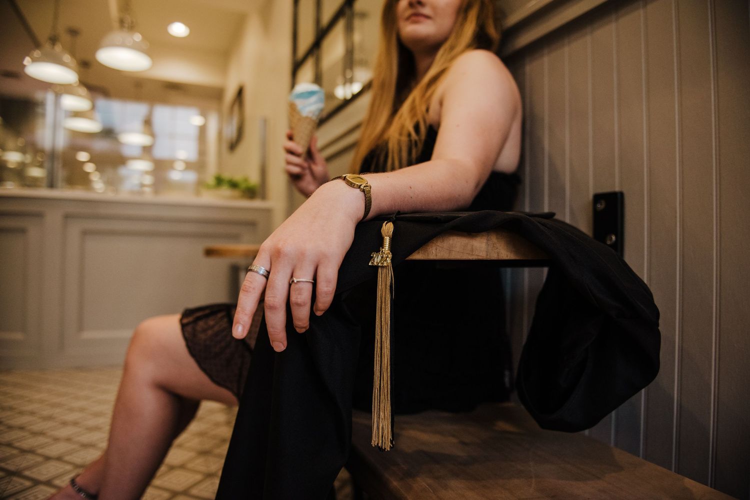 Close-up of a woman in a black dress sitting on a chair holding a graduation tassel and ice cream cone.