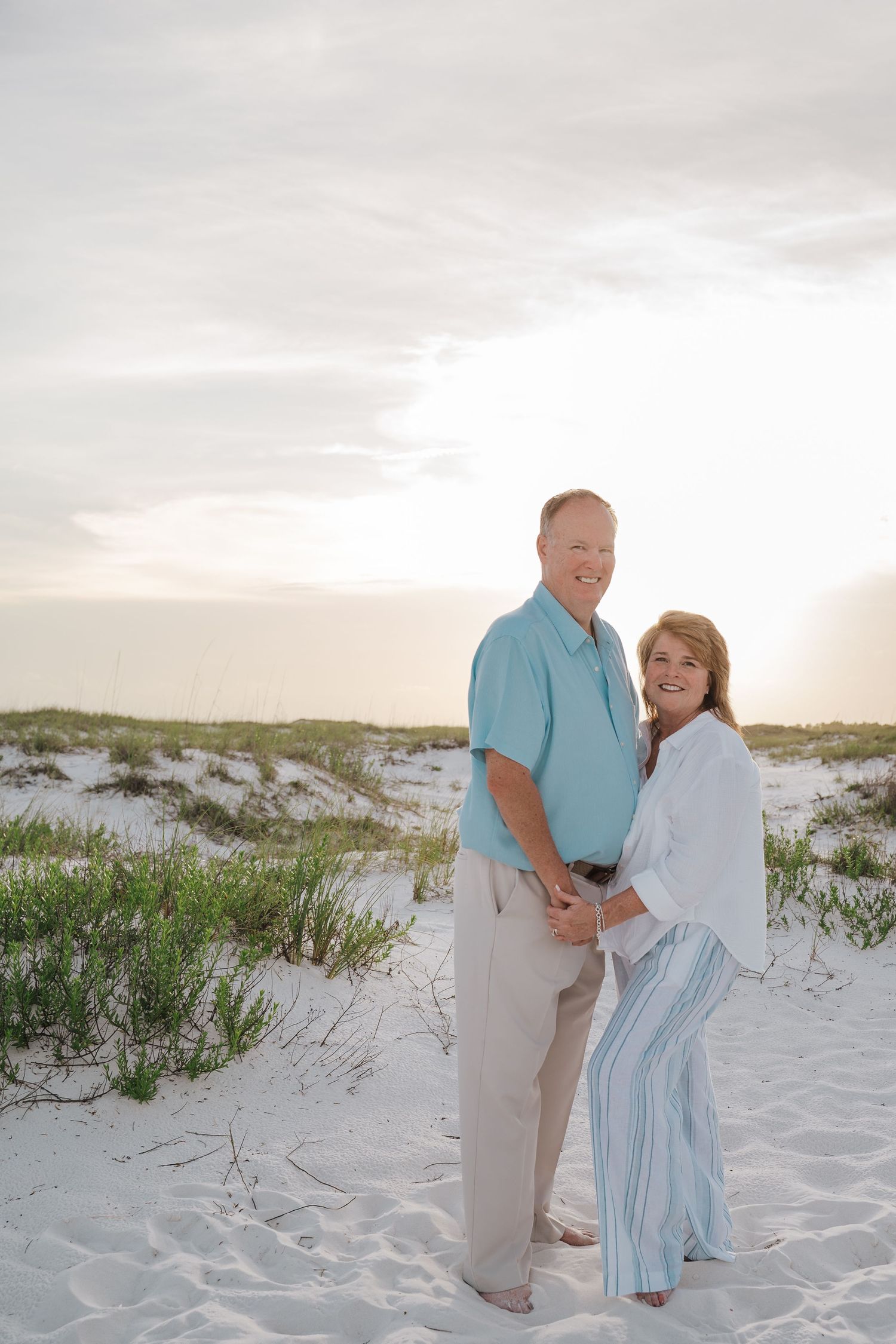 Happy mature couple holding hands and smiling together on a white sandy beach at sunset.
