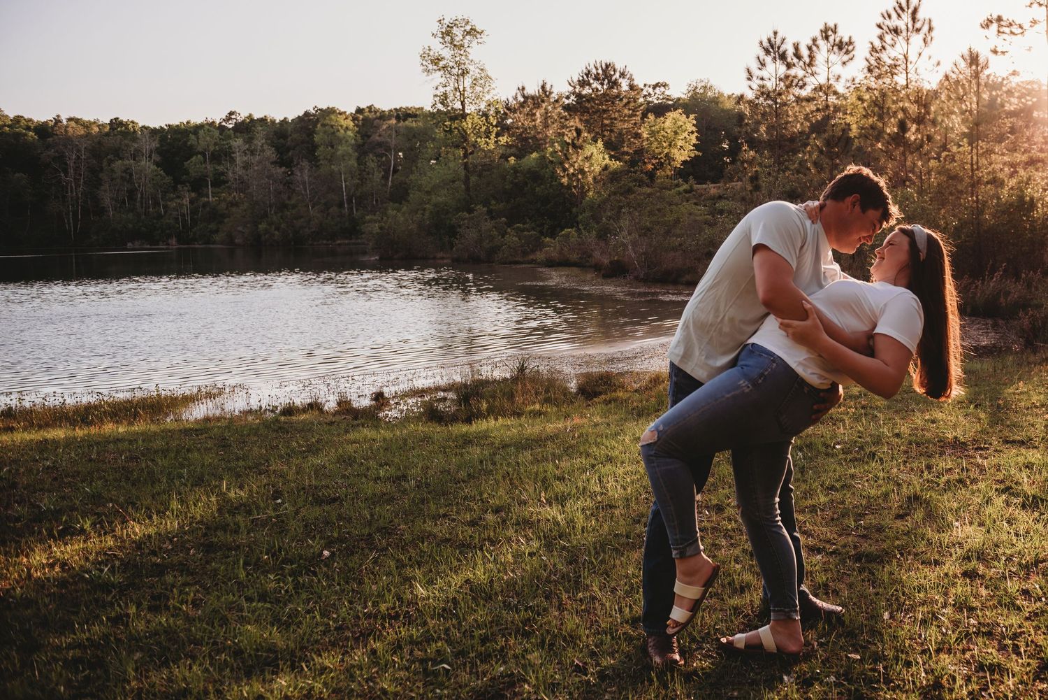 Couple sharing a romantic dip kiss by a serene lake at golden hour sunset.