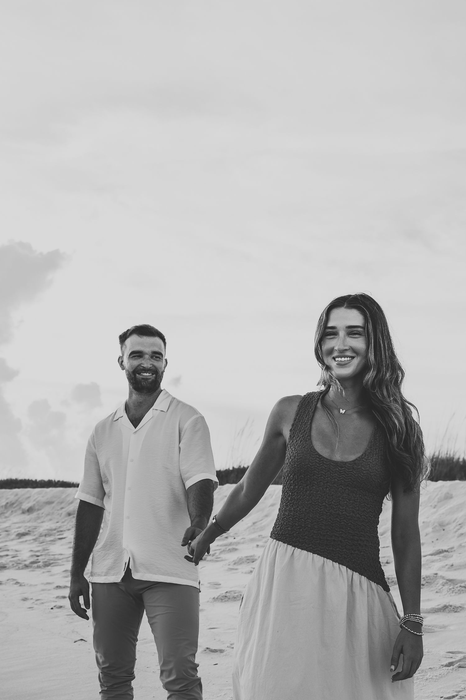 Black and white photo of a laughing couple holding hands while walking on a sandy beach.
