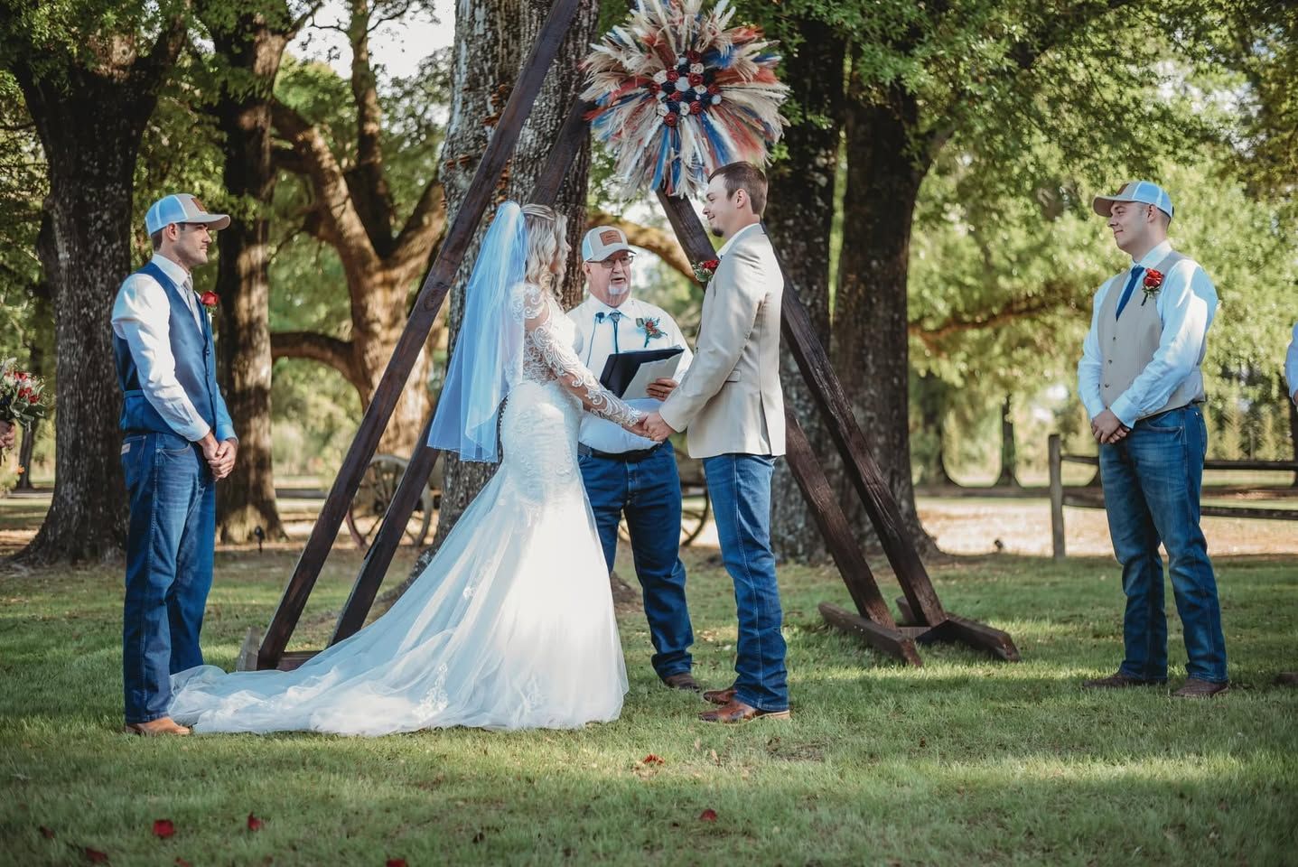 Outdoor rustic wedding ceremony under trees with bride, groom, officiant, and two groomsmen at altar.