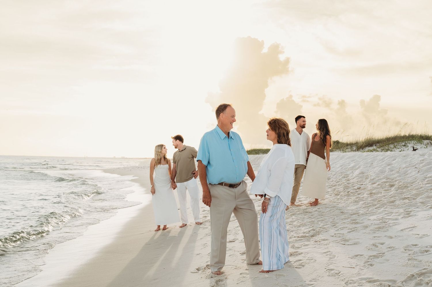 Family group enjoys a golden hour beach stroll along the shoreline with sand dunes nearby.