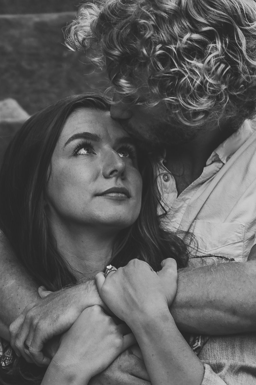 Black and white photo of a couple in an intimate embrace, woman gazing up lovingly at curly-haired man.