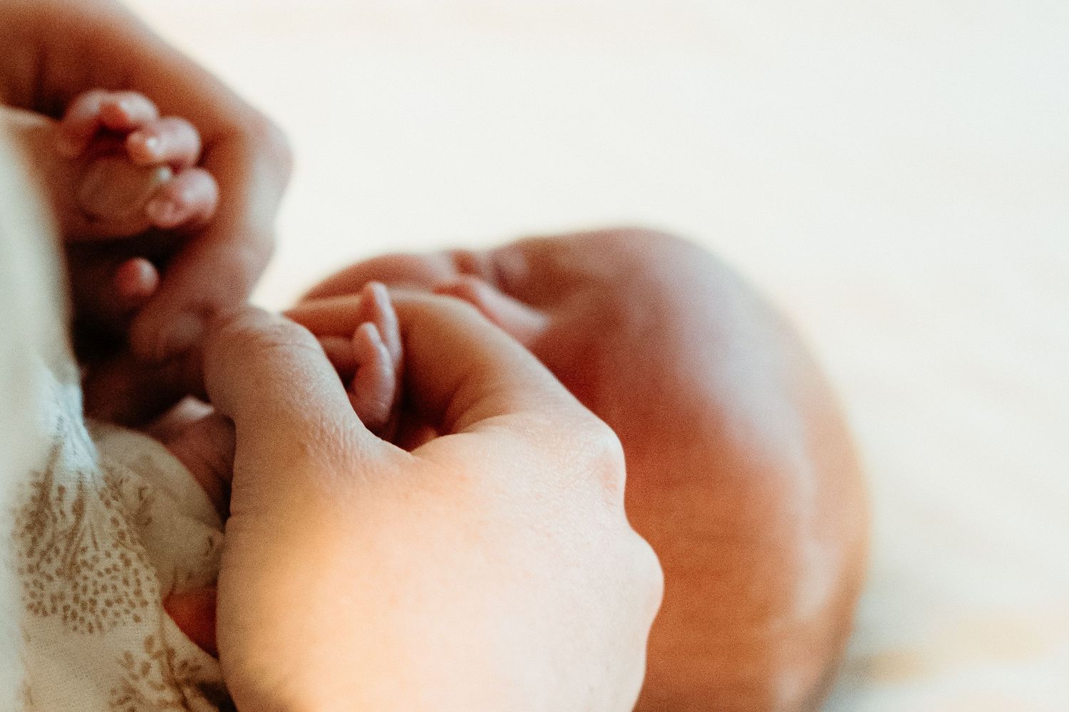 Close-up of an adult hand gently holding a newborn babys tiny feet on a soft white blanket.