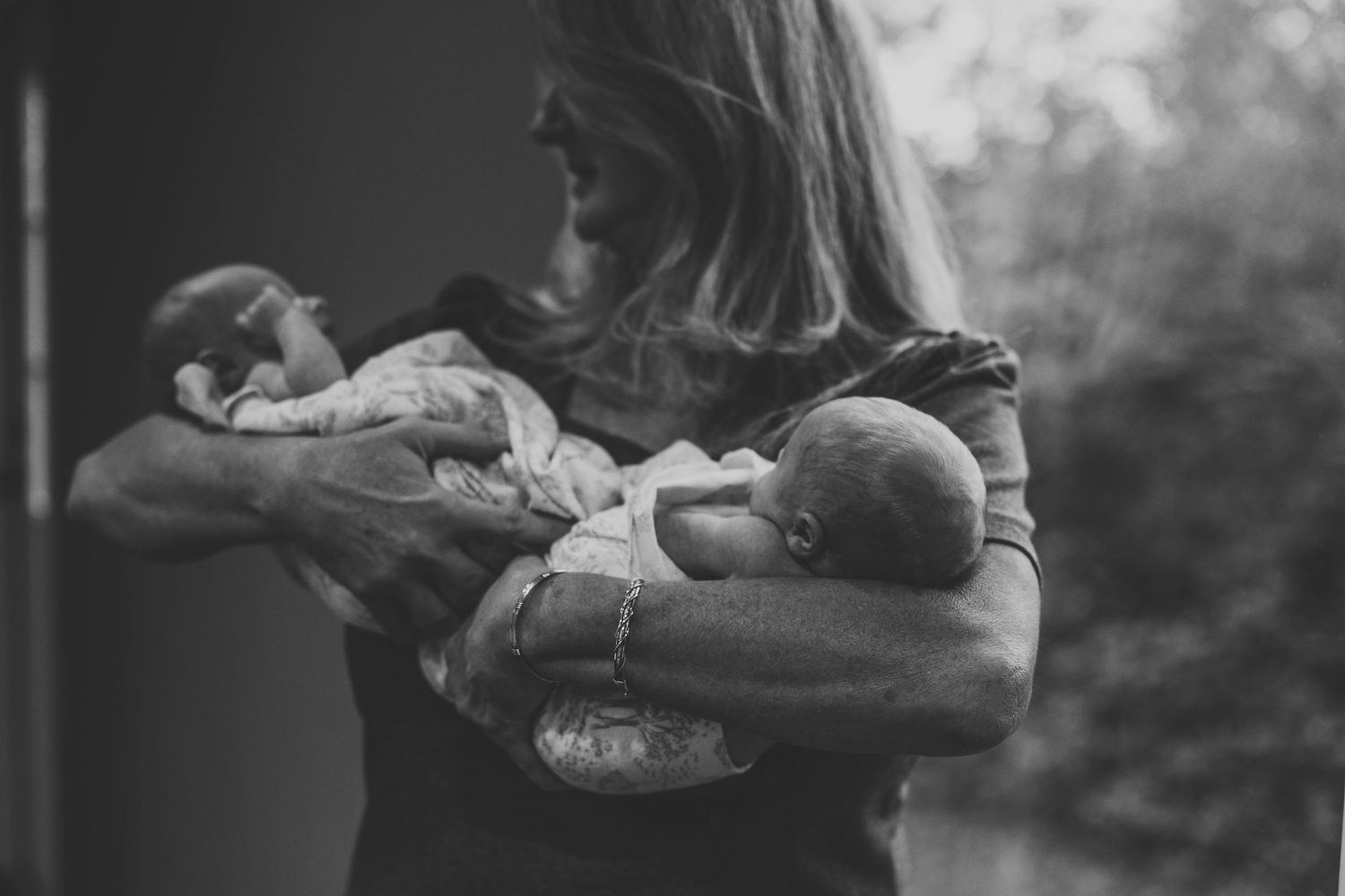 Black and white photo of mother holding two newborn twins in her arms.