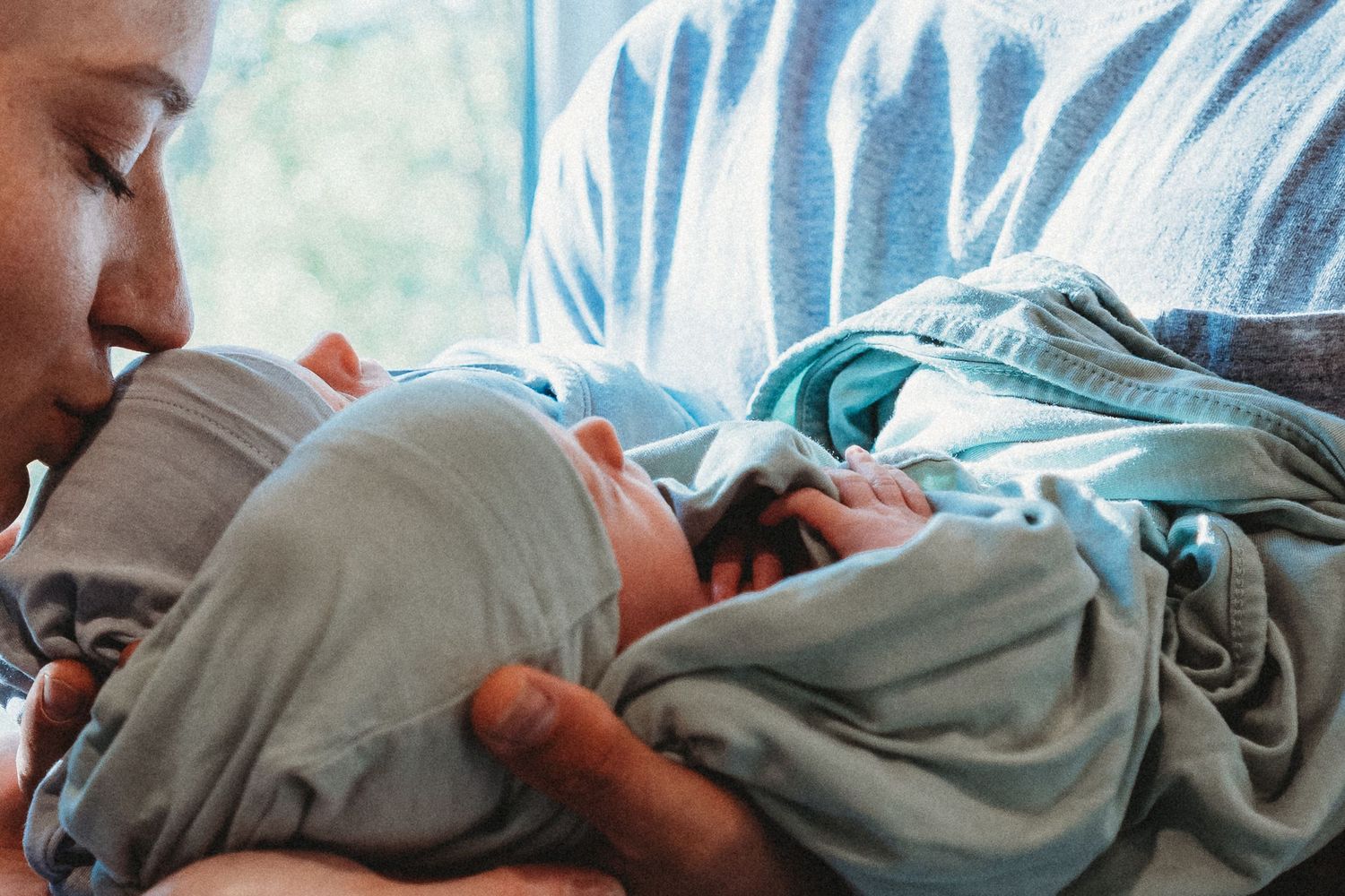 Mother tenderly gazing at her swaddled newborn baby in a blue blanket.