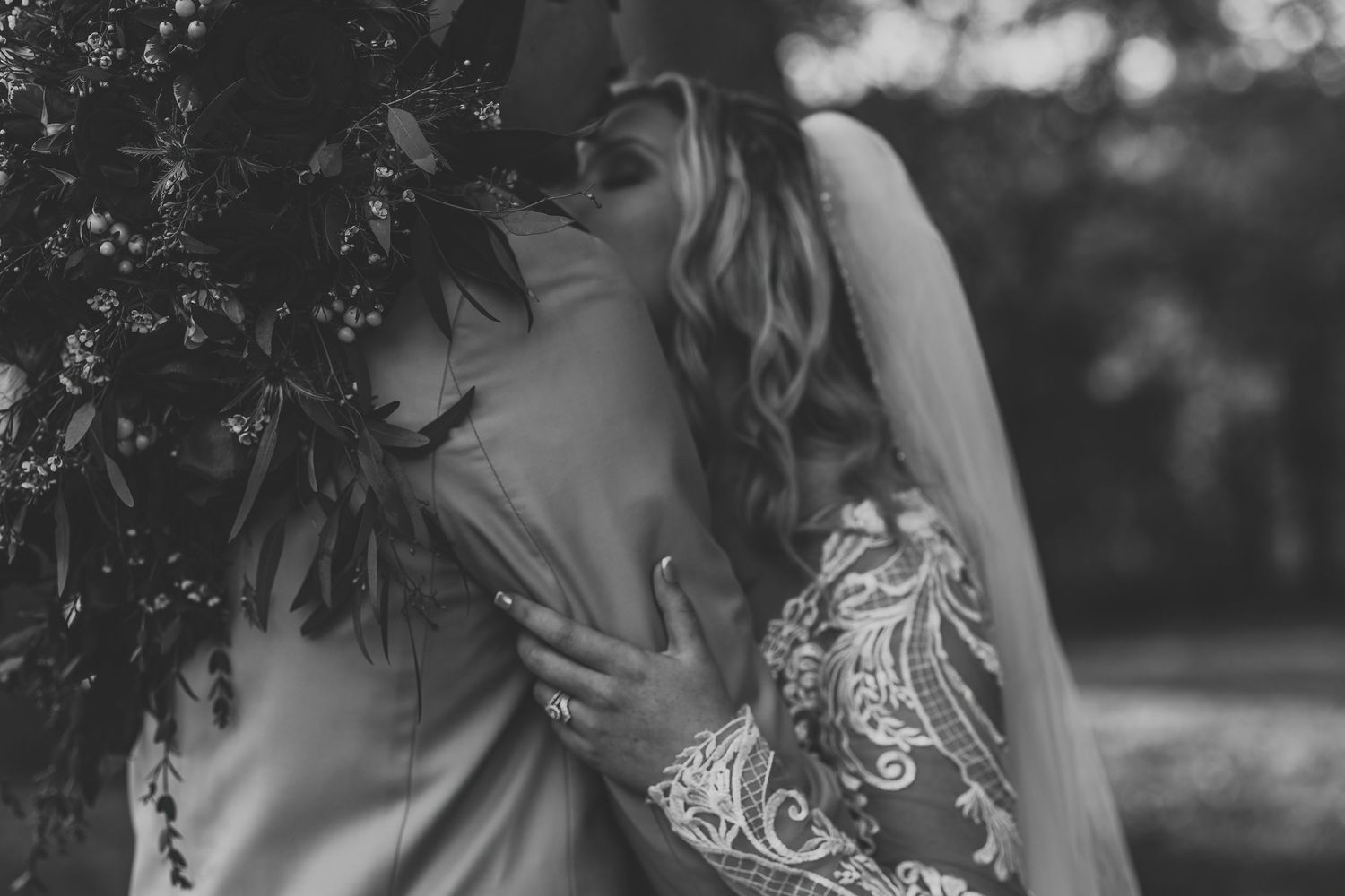 Black and white close-up of bride and groom sharing a kiss beneath a floral wedding arch.