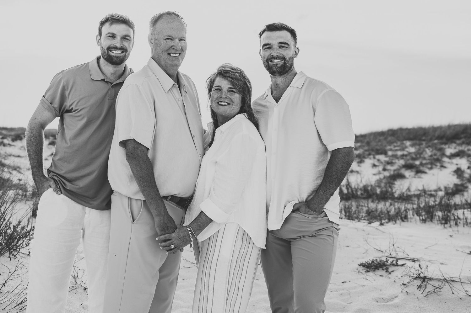 Black and white photo of a happy family of four posing together on a sandy beach.