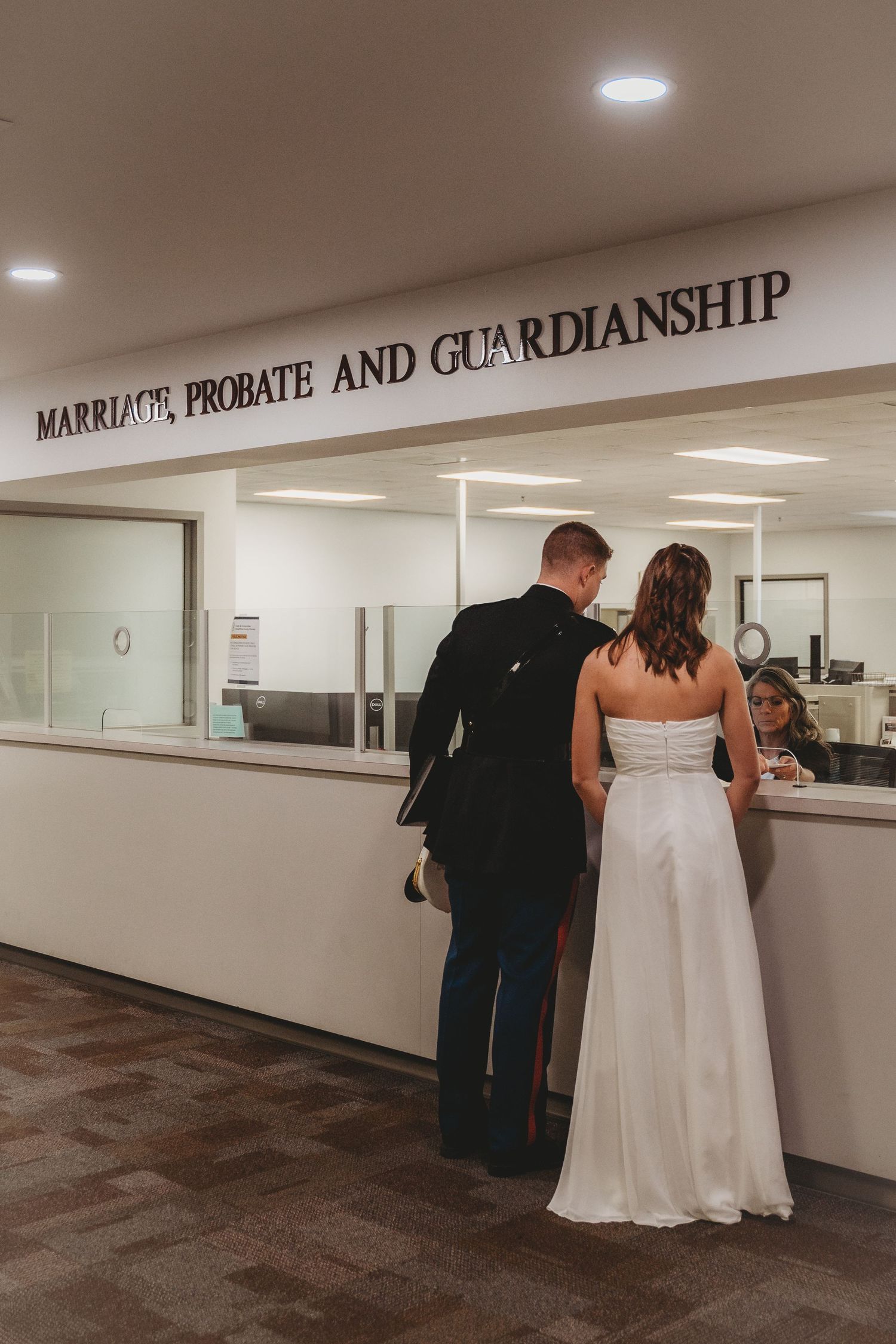 Couple in wedding attire at a Marriage, Probate and Guardianship courthouse counter obtaining their marriage license.