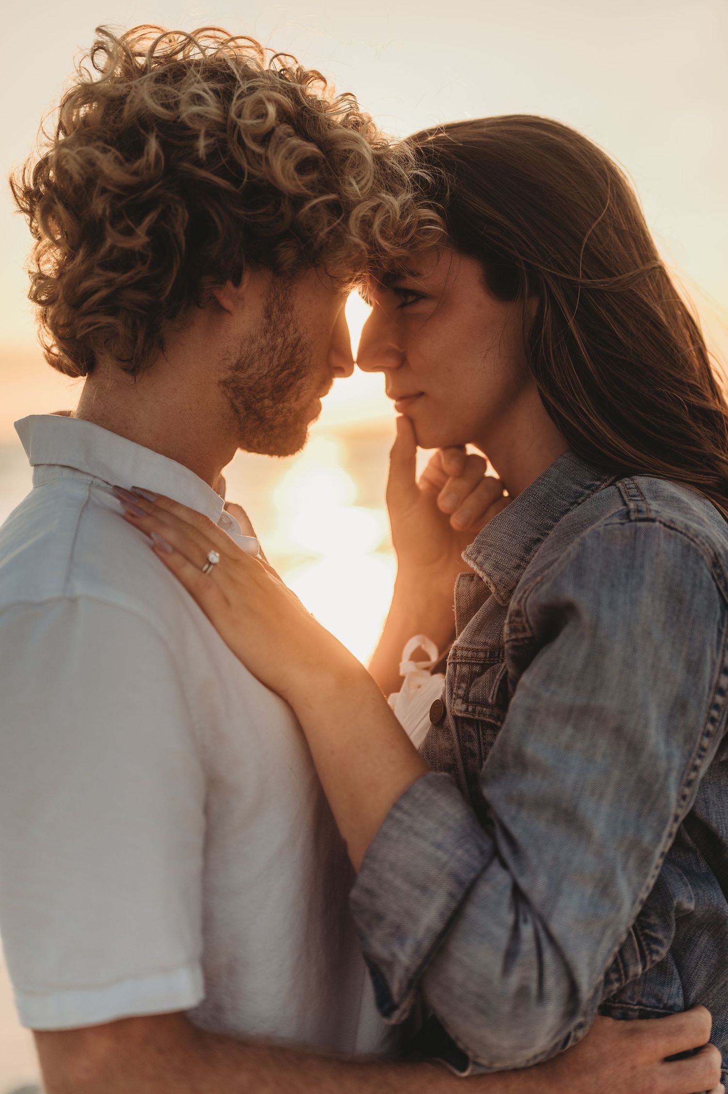 Couple sharing an intimate moment at golden hour sunset, woman wearing engagement ring.
