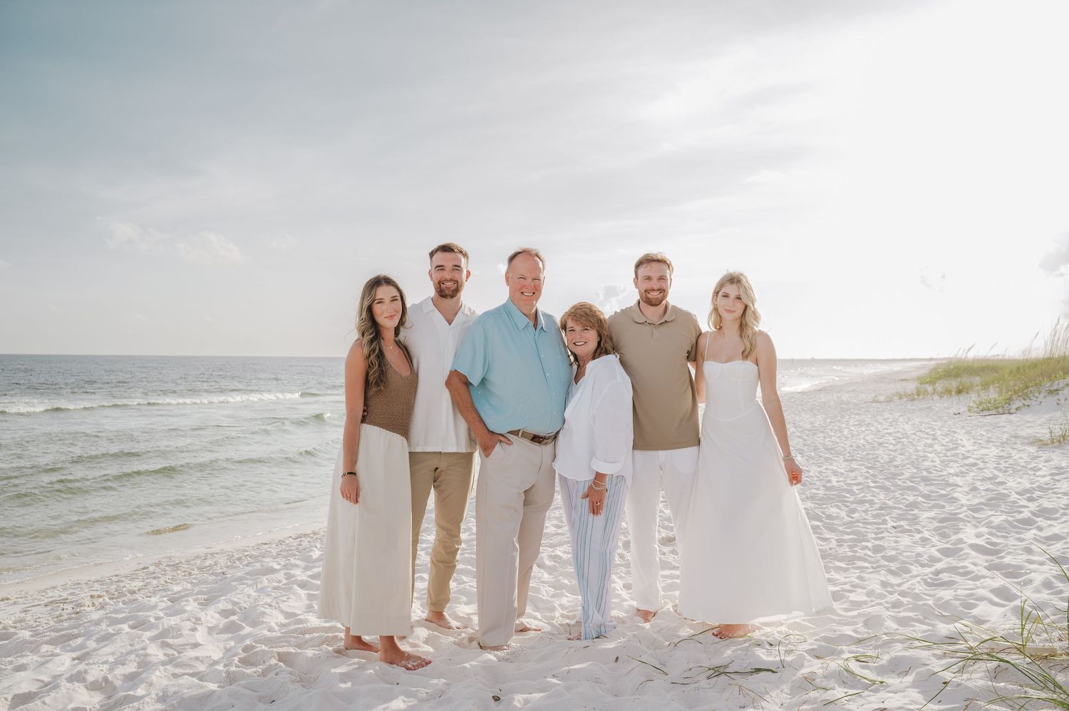Happy family of six smiling together on a bright white sand beach near sand dunes.
