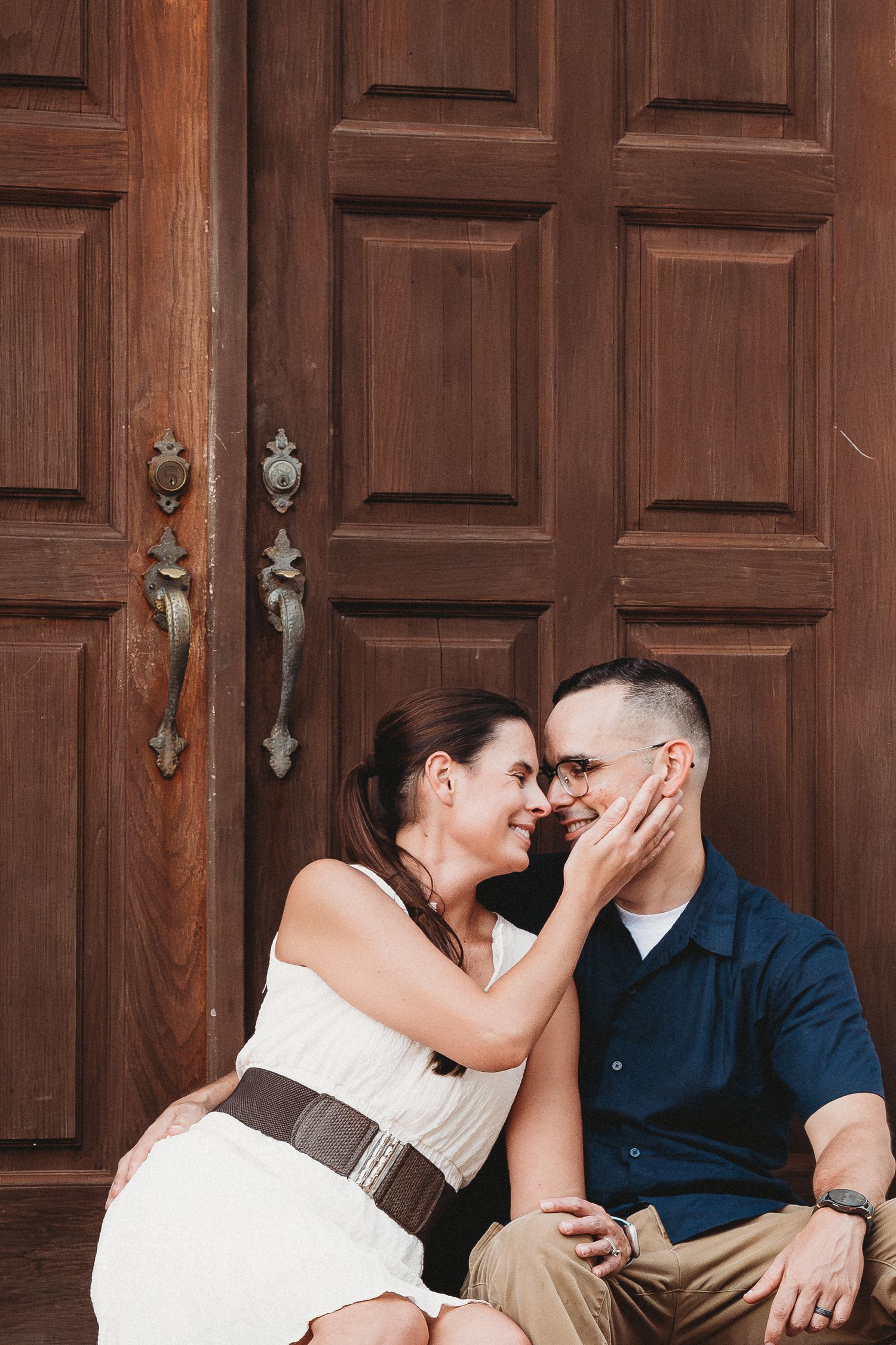 Couple sharing a tender moment sitting before large ornate wooden double doors.