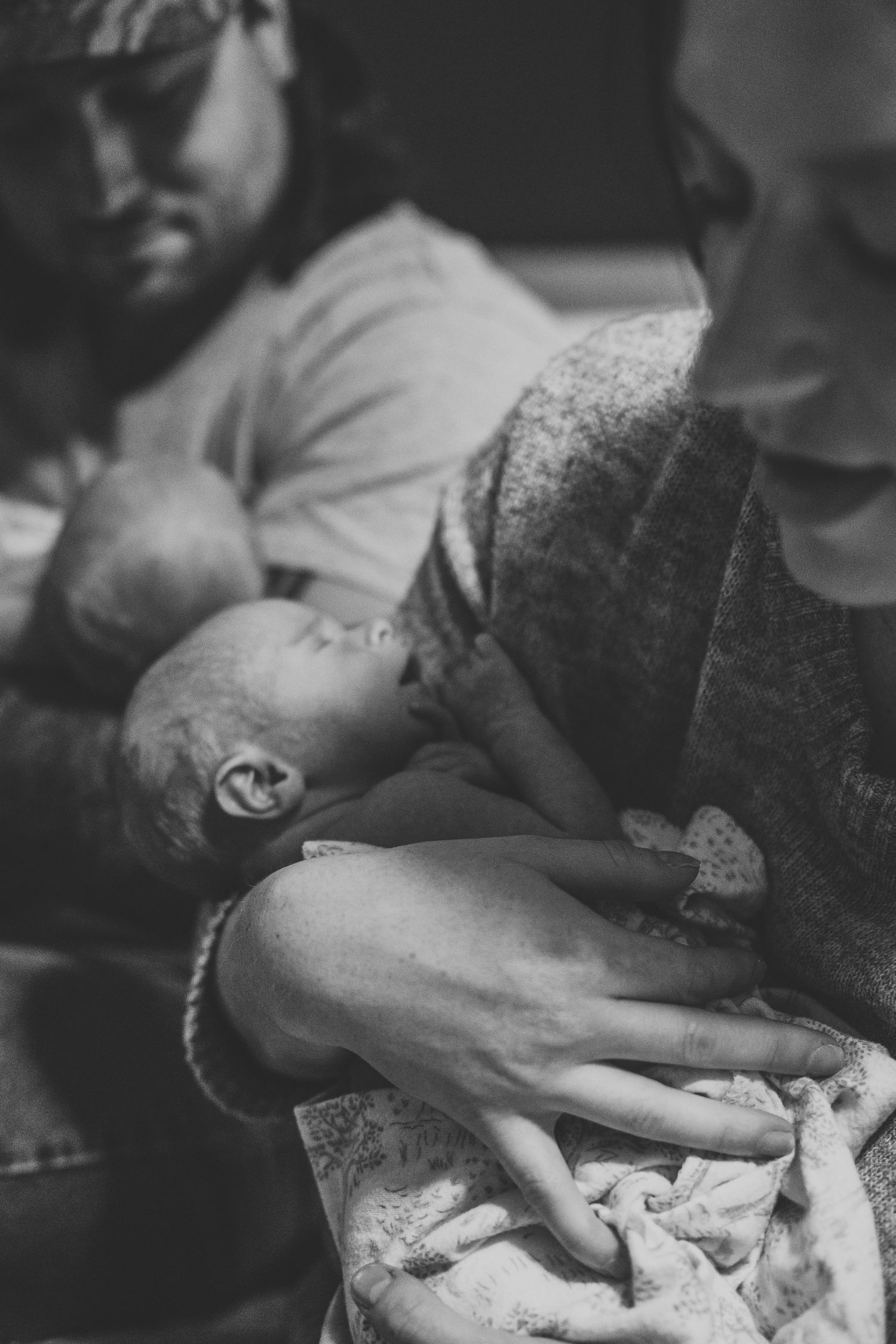 Black and white image of parents tenderly cradling their sleeping newborn baby together.
