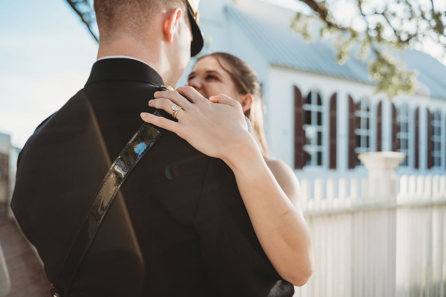 Bride resting her hand on groom's shoulder during romantic outdoor wedding ceremony near white fence.