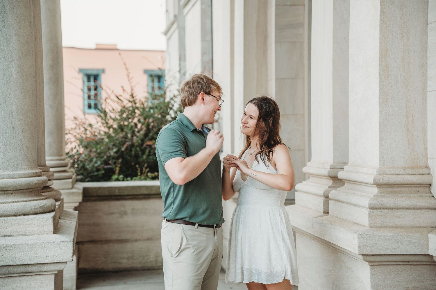 Couple sharing a romantic moment between white columns, man in green polo and woman in white dress.