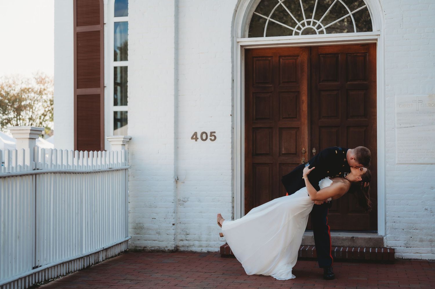 Bride and groom share romantic dip kiss outside white brick building with brown door numbered 405.