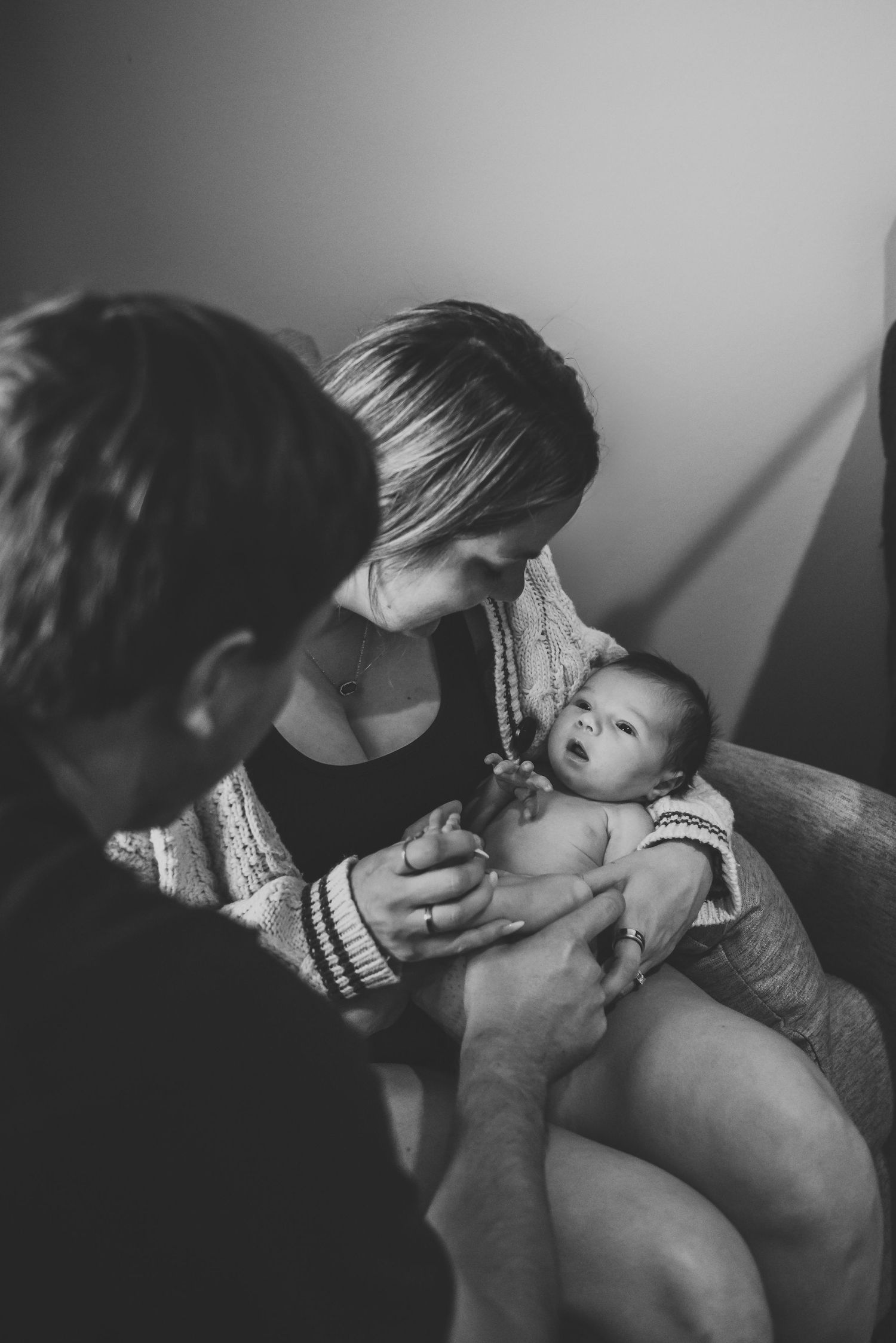 Black and white photo of new parents admiring their alert newborn baby together.