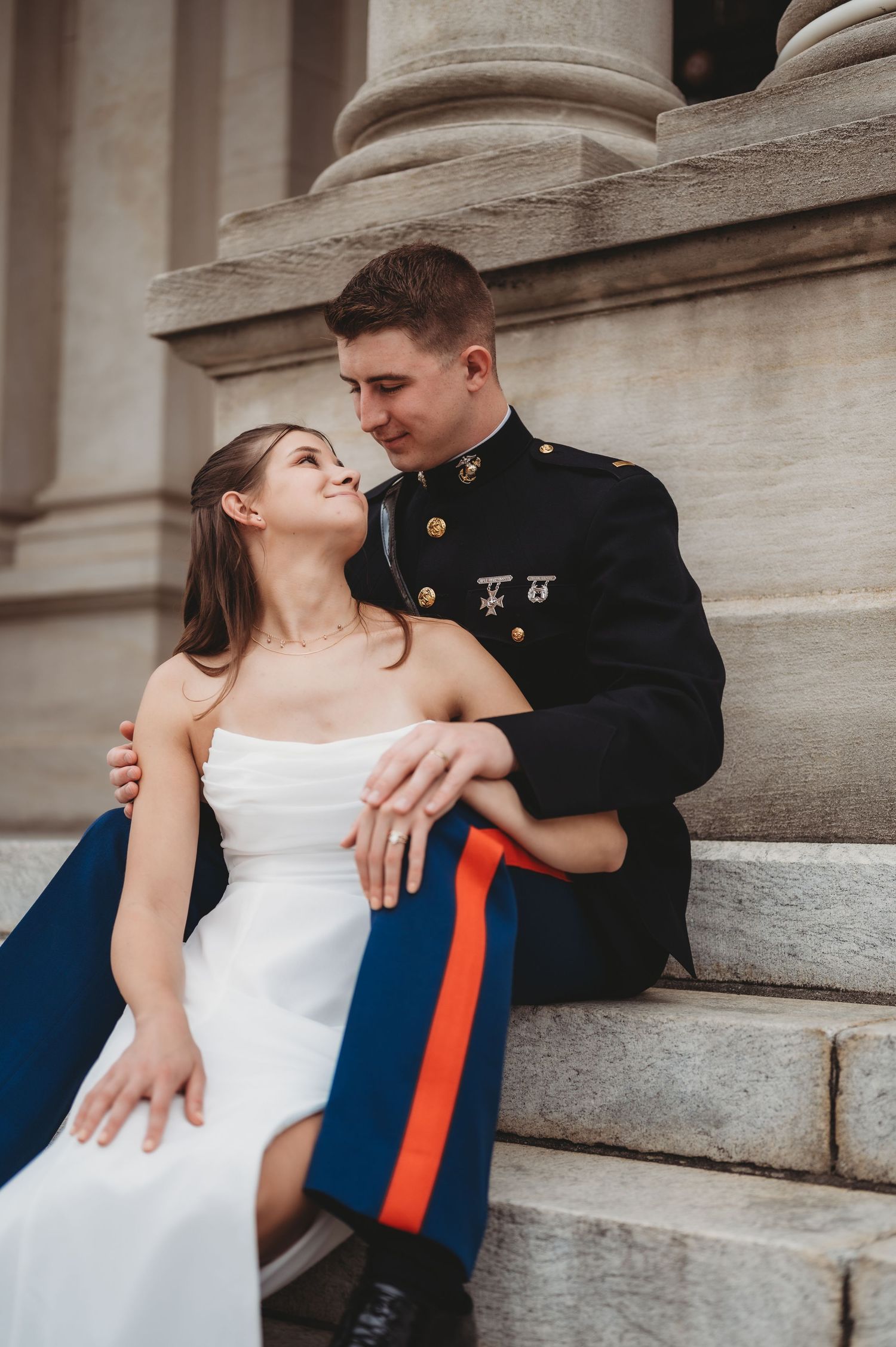 Marine groom and bride sit on stone steps sharing a tender moment beside grand columns.