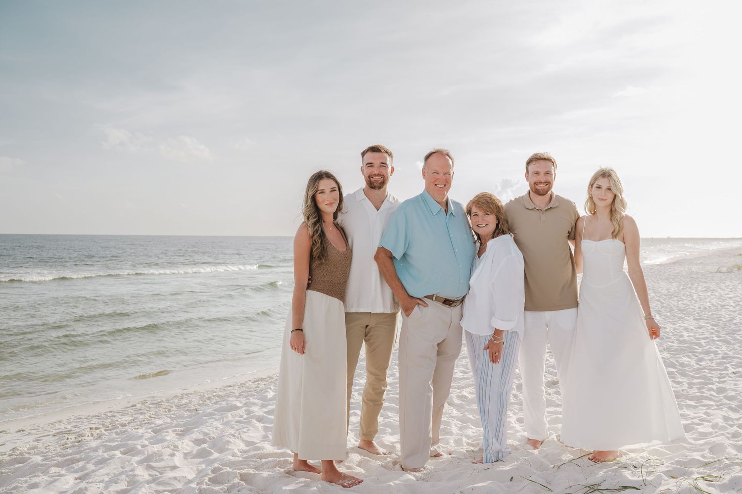 Family of six posing together on a white sand beach with ocean waves in the background.
