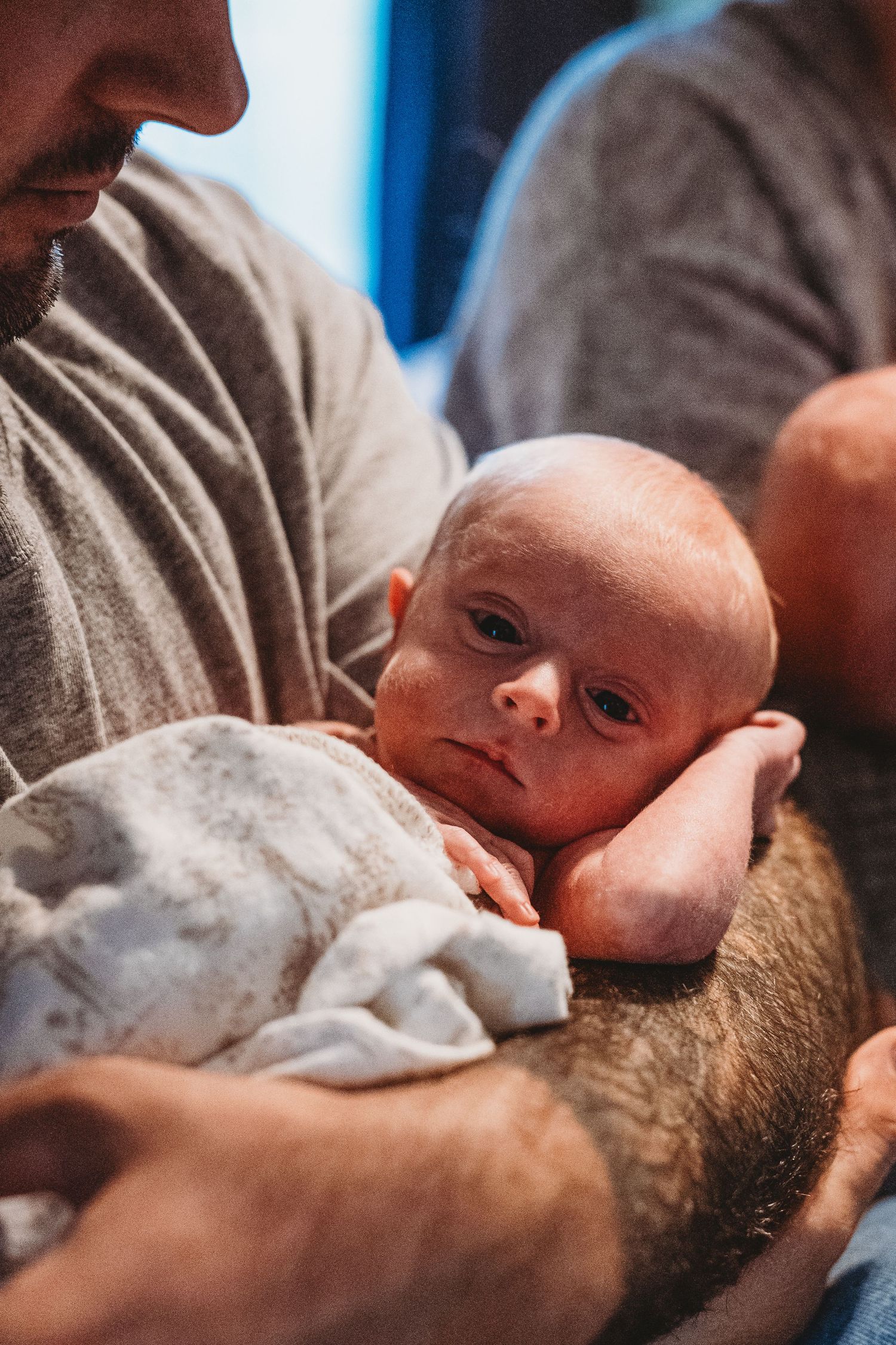 Close-up of bearded father cradling alert newborn baby on his forearm.